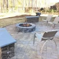 Patio with a fire pit, seating, and a stone wall in an outdoor setting.