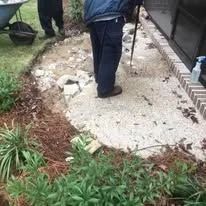 Person shoveling gravel on a concrete surface next to a building.