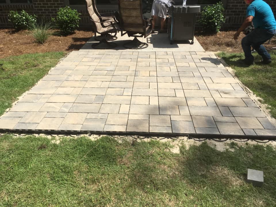 Workers installing stone pavers on a patio. Green grass surrounds the patio.