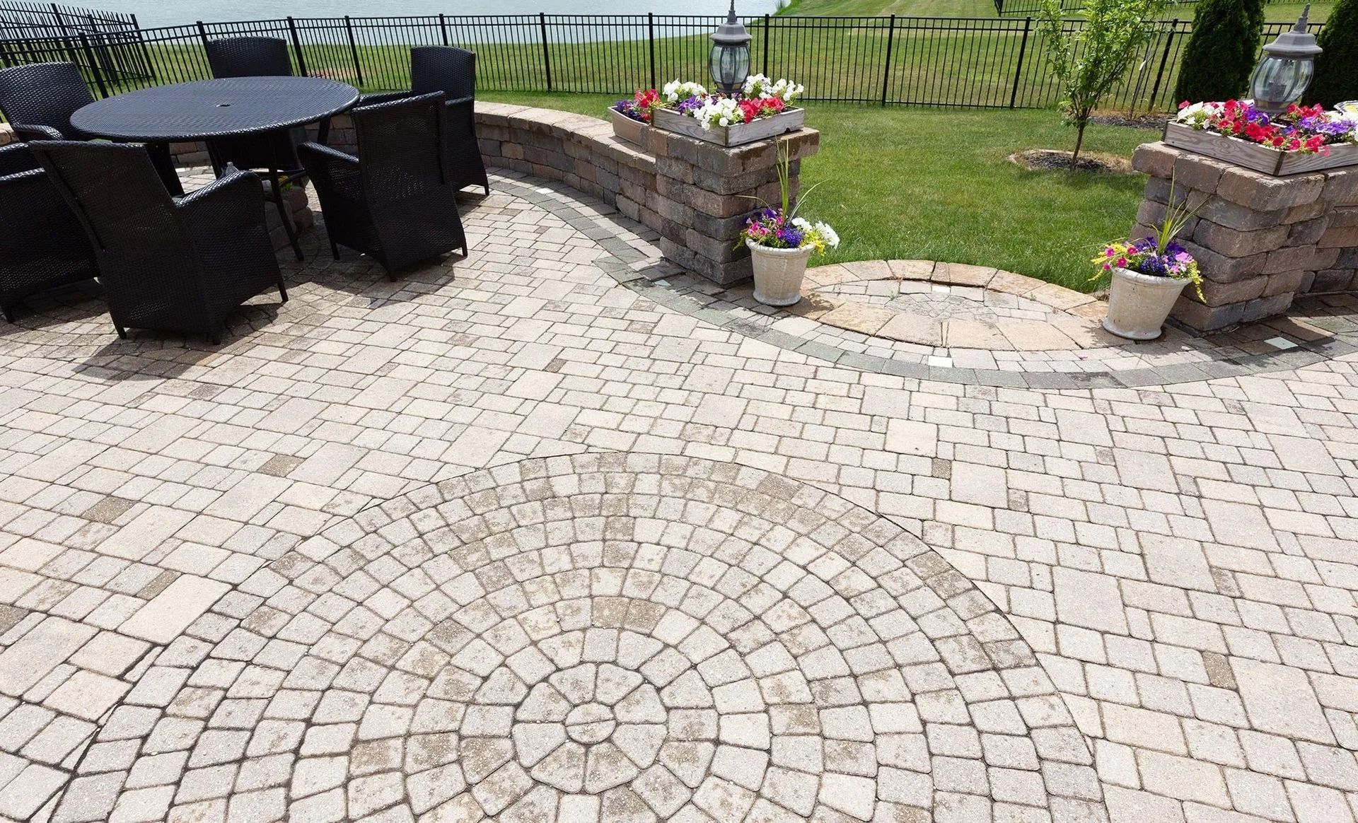 Brick patio with circular design, outdoor furniture, and flower-filled planters.