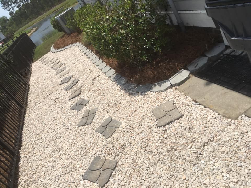 A gravel pathway with stepping stones leads to a landscaped area, bordered by a fence and a building.