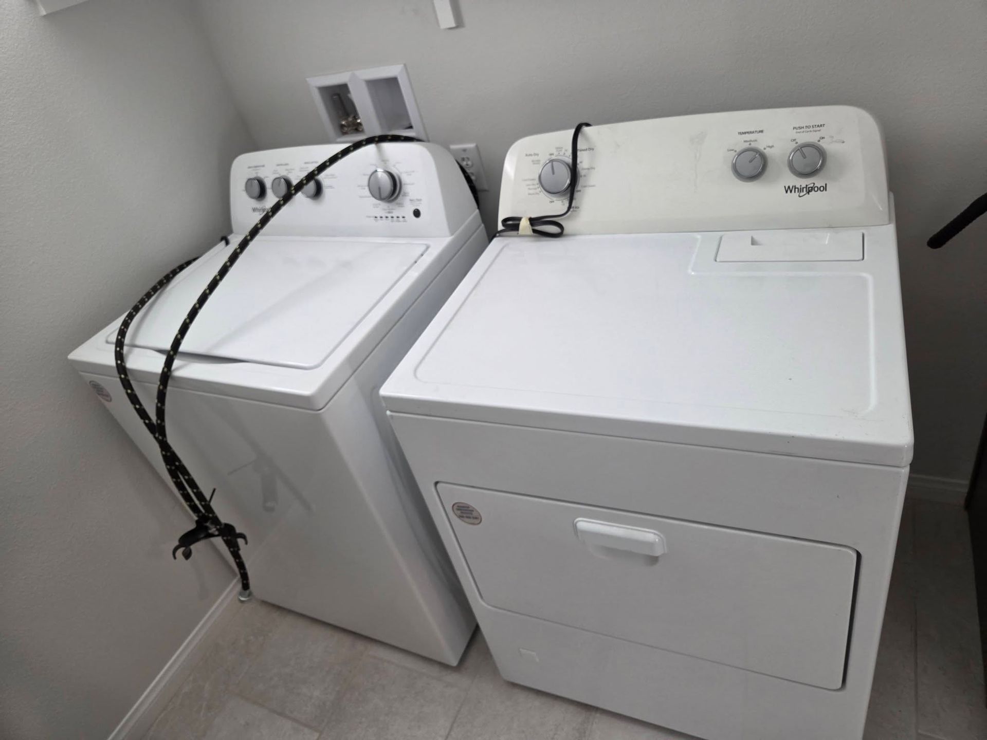White washer and dryer side by side in a laundry room, with cords draped over the washer.
