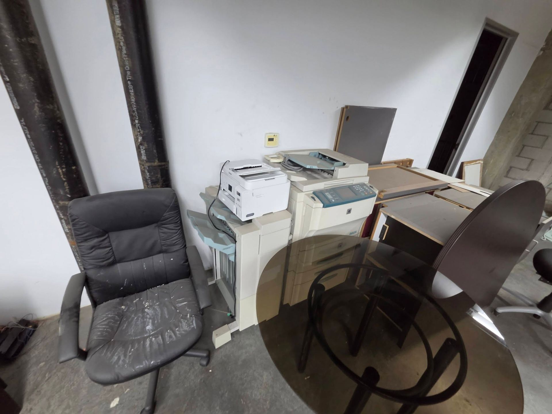 Cluttered office corner with chairs, desk, and stacked printers against a wall