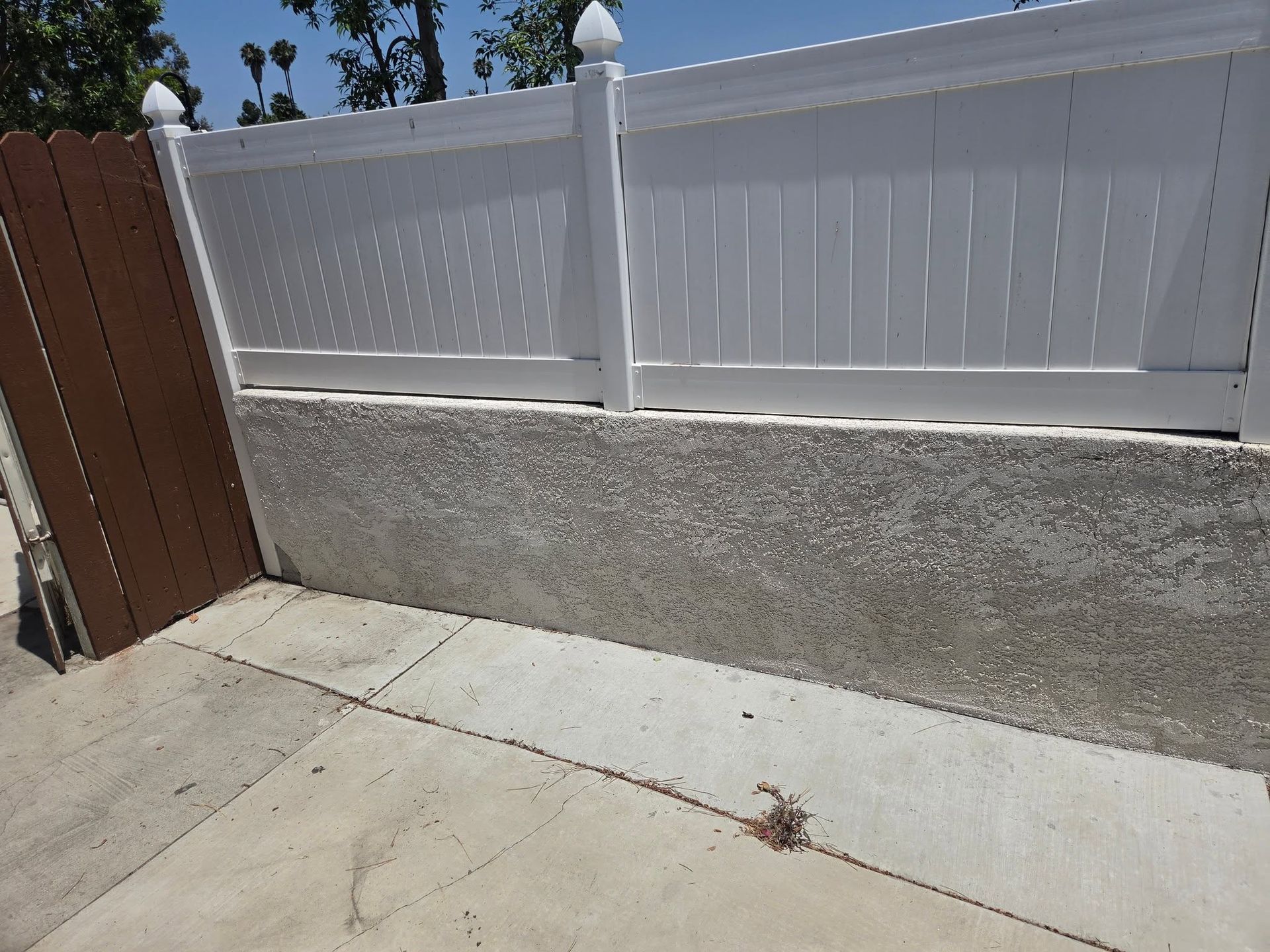 Concrete yard with a white vinyl fence and a brown wooden fence under a clear blue sky