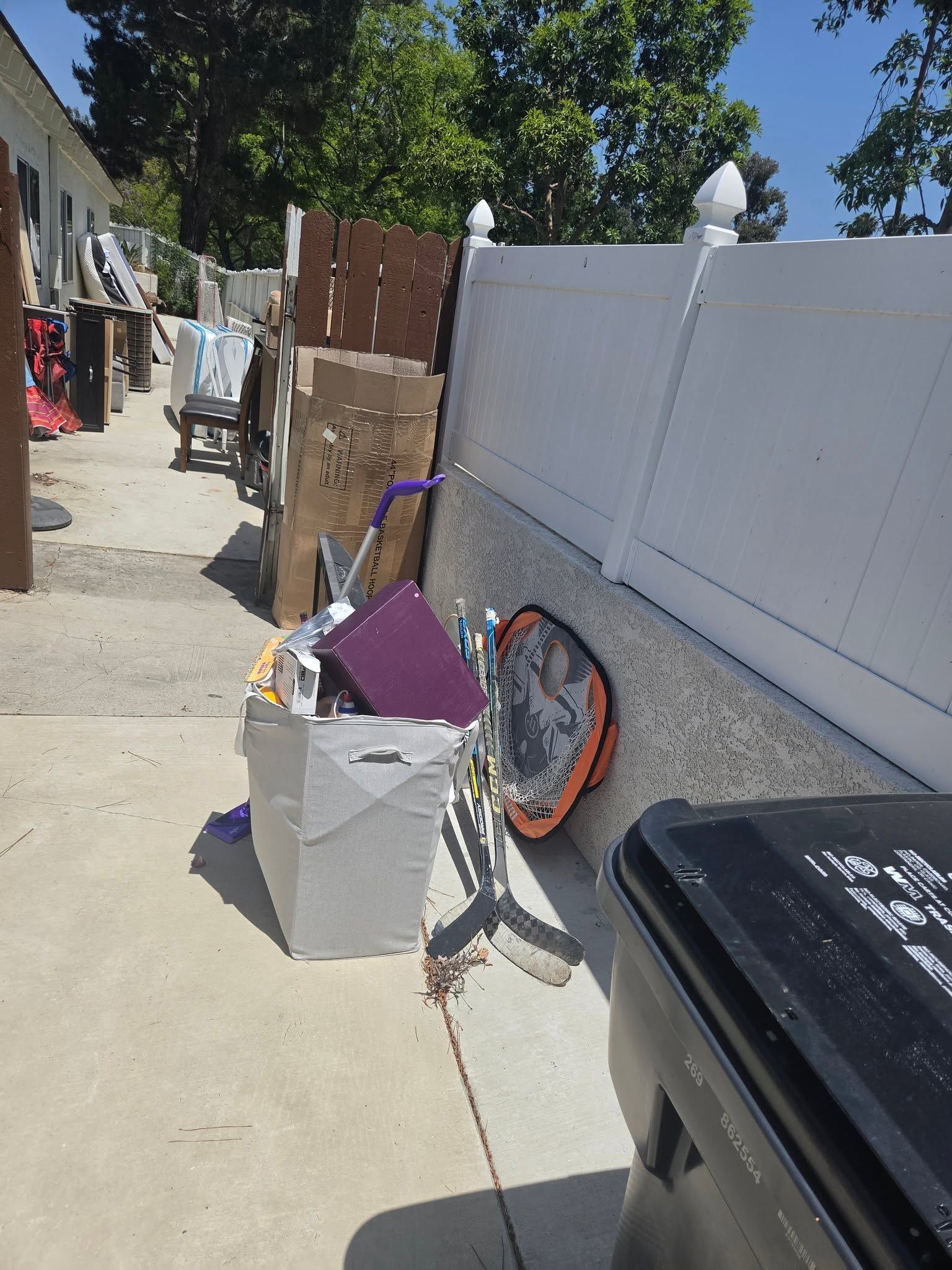 Side yard walkway with scattered items, a white fence, and a trash bin in the foreground.