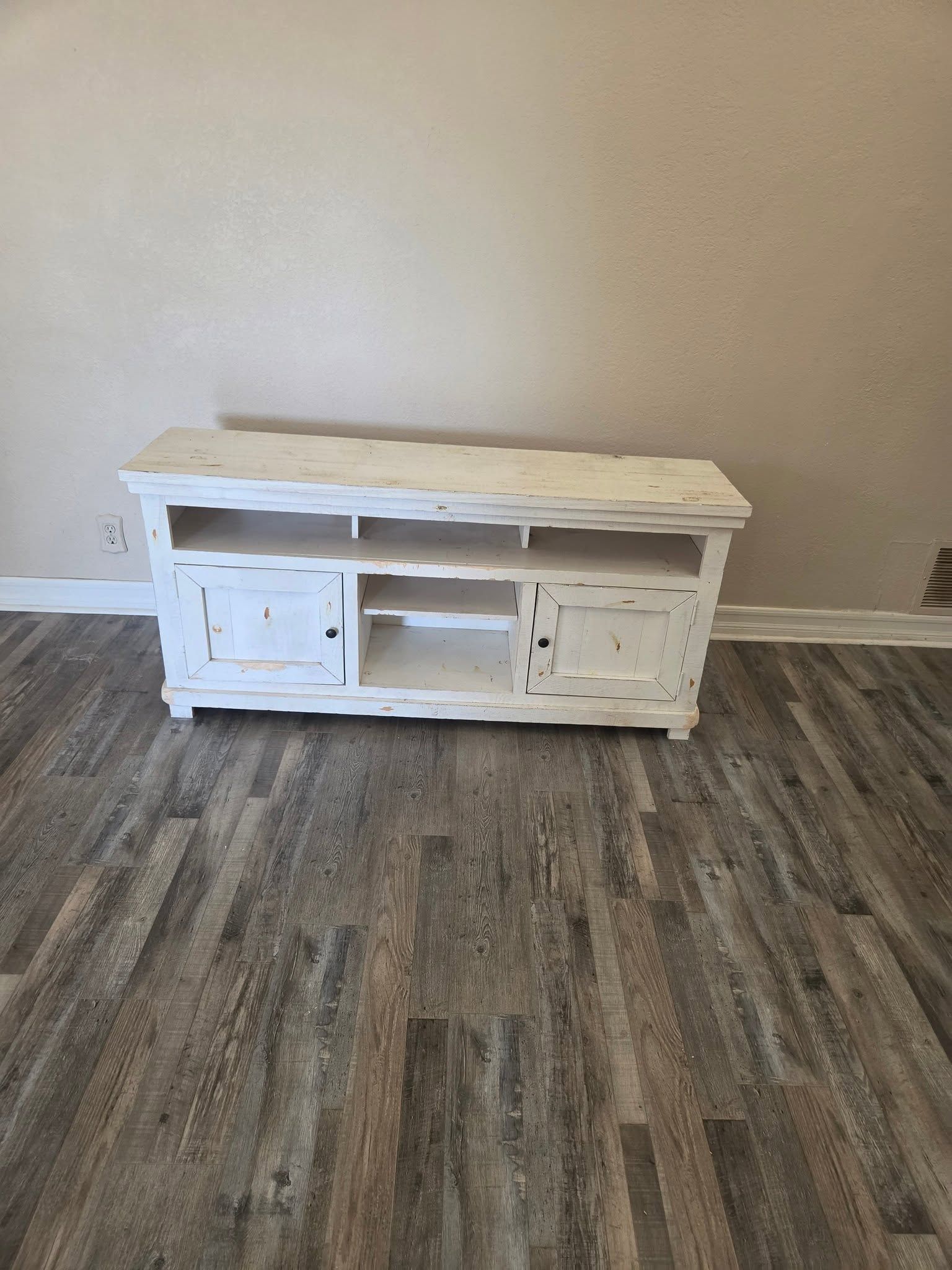 White distressed TV stand against a beige wall on wood-look flooring.