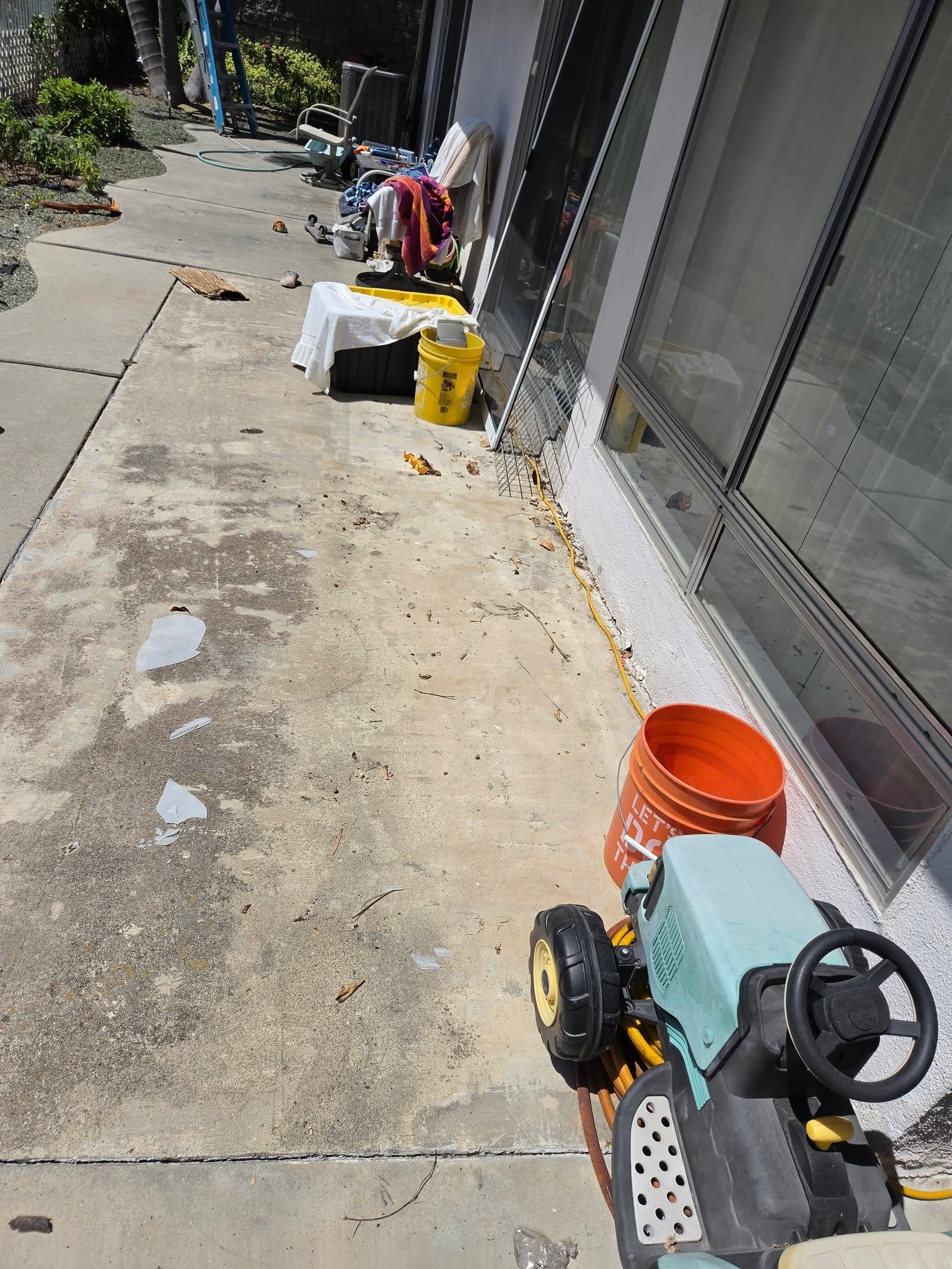 Outdoor walkway beside glass storefront with buckets, cleaning supplies, and a small cart.