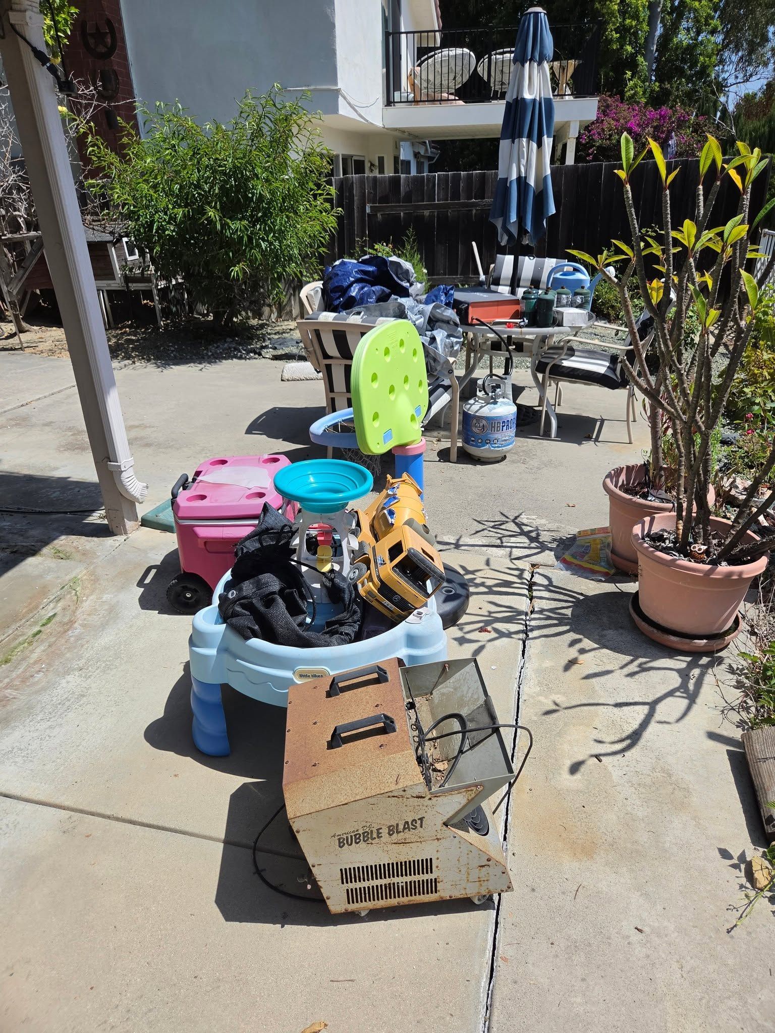 Miscellaneous items stacked on boxes and bins on a sunny outdoor patio walkway