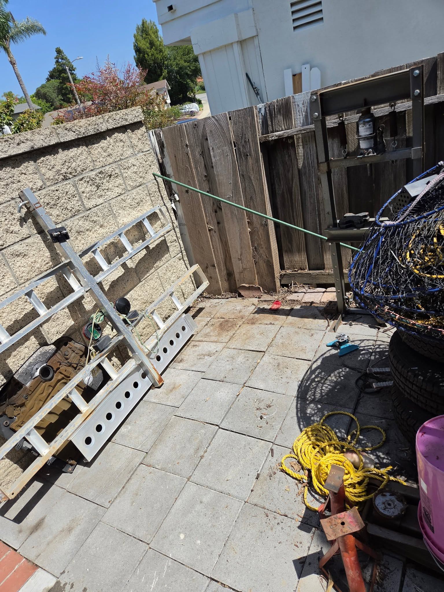 Sunlit patio with stone wall, wooden fence, hanging clothesline, and yellow hose reel on tiled floor