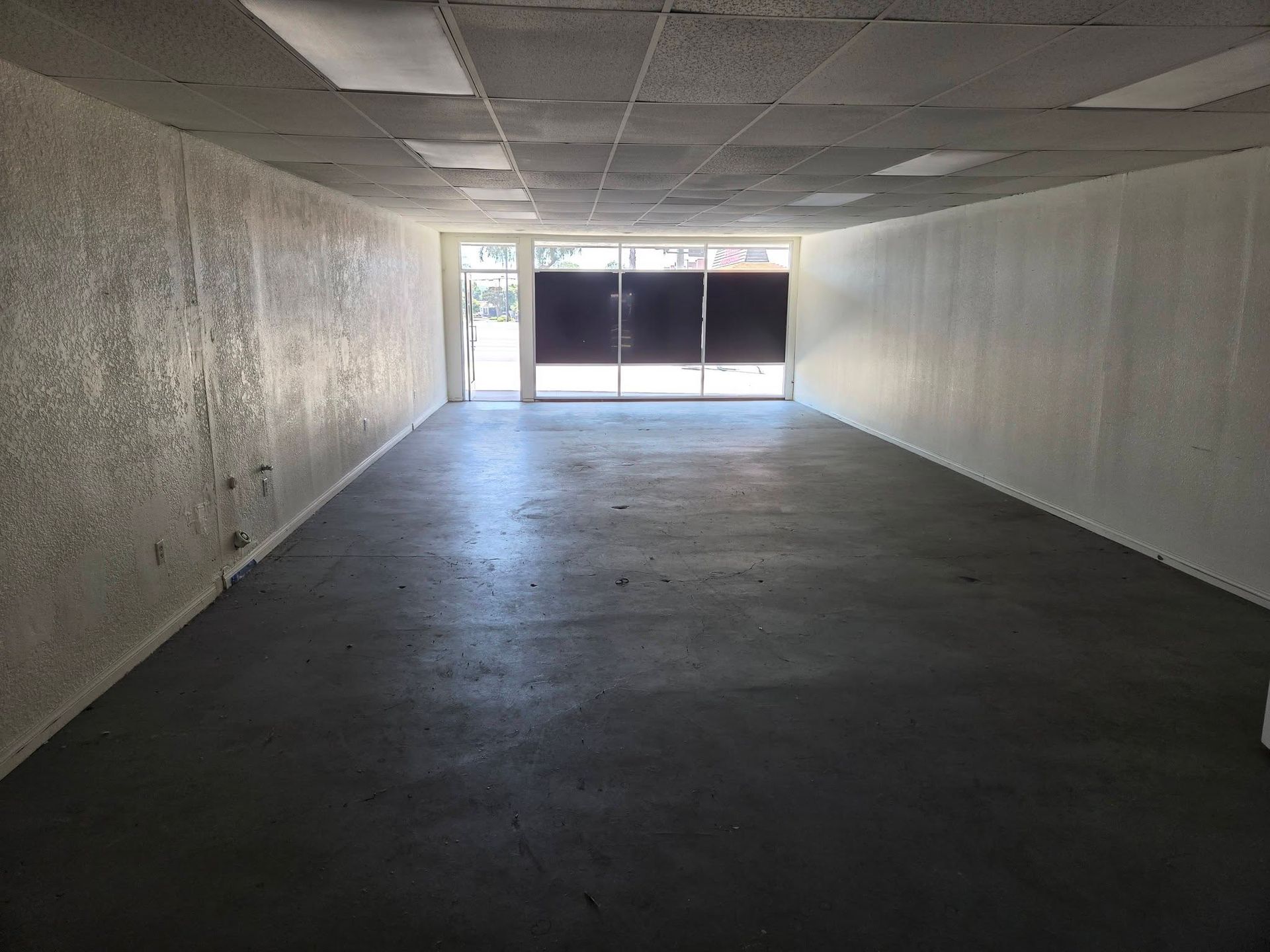 Empty long white room with dark floor and large windows at the far end.