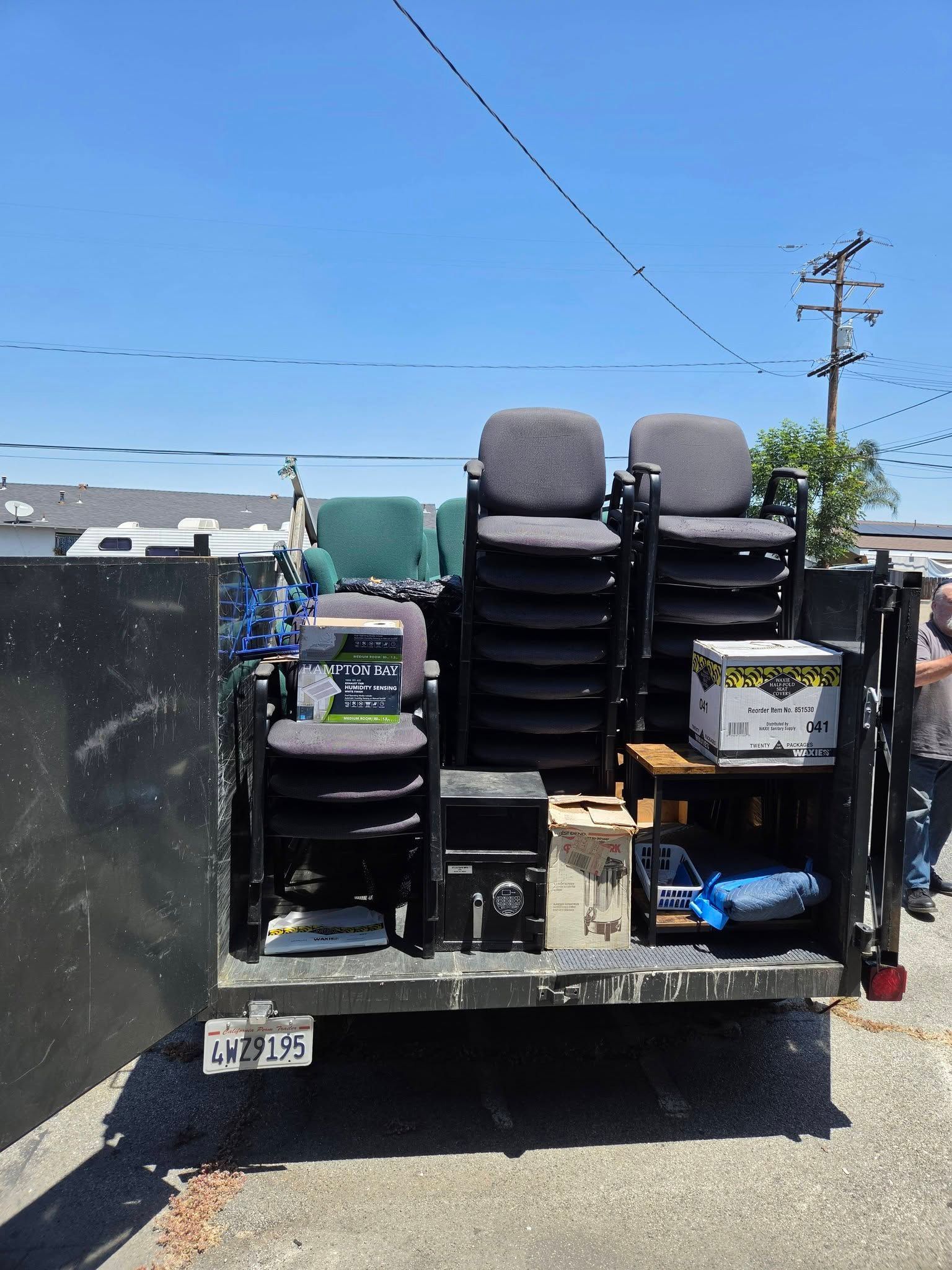 Equipment stacked on a trailer in a sunny outdoor lot, with tires, bins, and tools visible.