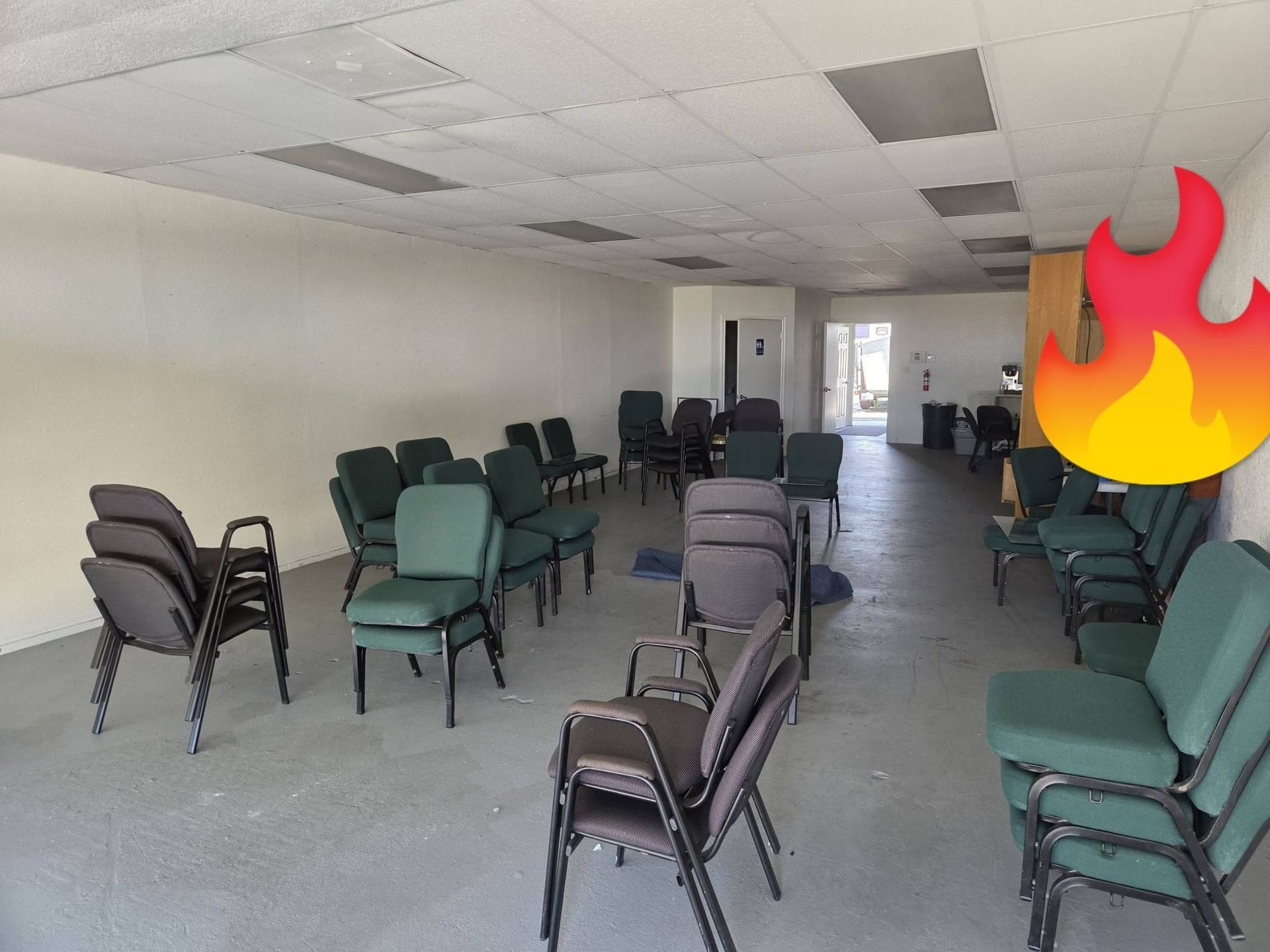 Empty room with rows of stacked chairs and a ceiling fire damage or flame icon near the doorway.