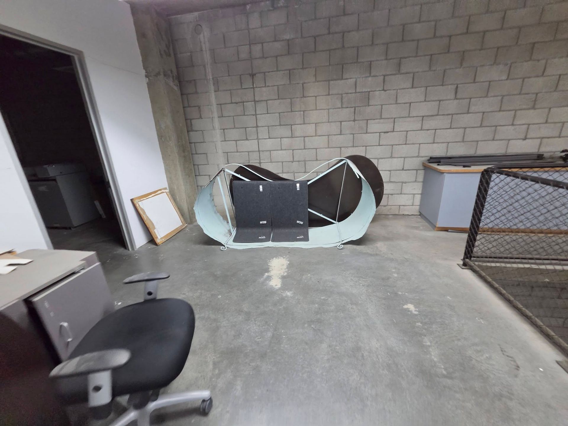 Empty industrial room with cinder block walls, a tipped cabinet, and a chair in the foreground.