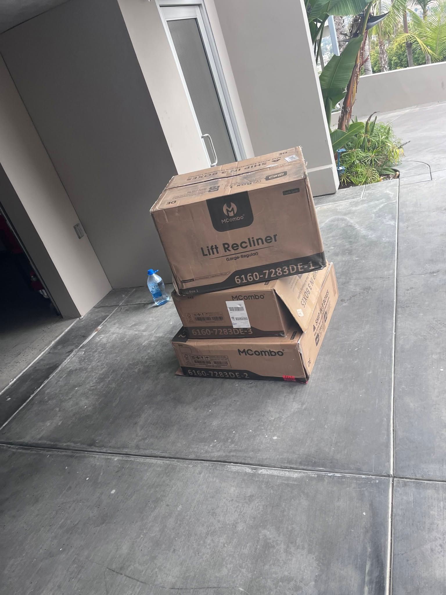 Two cardboard boxes stacked on a sidewalk beside a building entrance