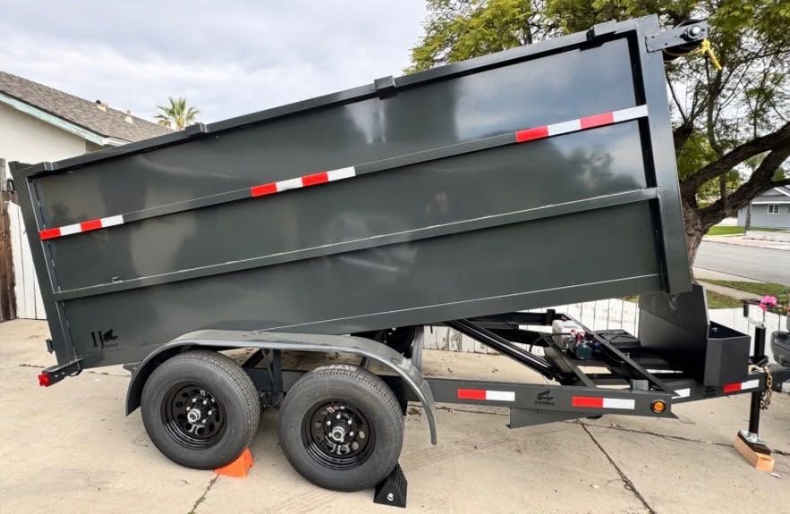 Black dump trailer with tandem wheels parked on a driveway with orange wheel chocks