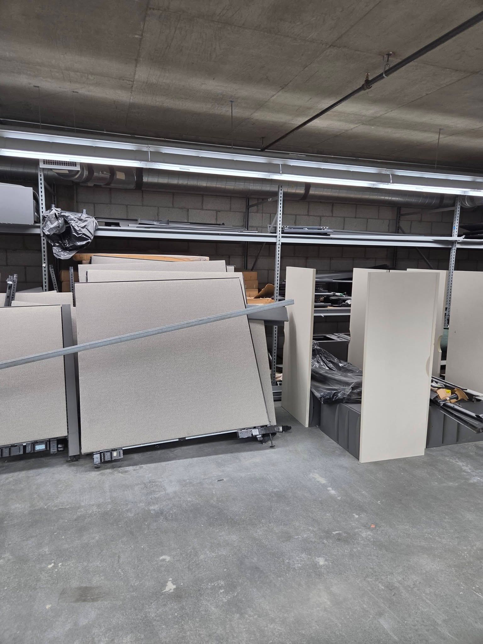 Warehouse with stacks of large panels on carts beside machinery under fluorescent lights