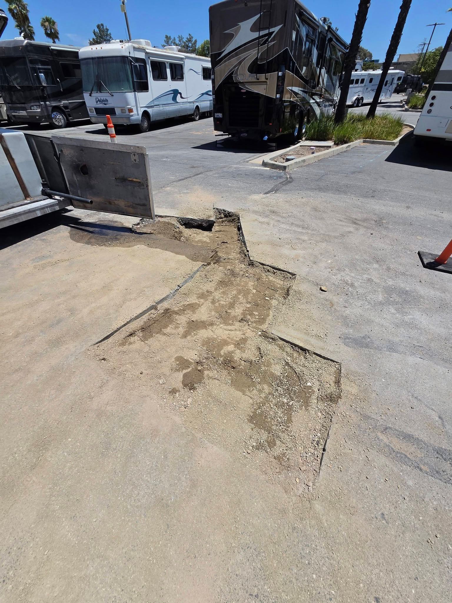 Cracked concrete sidewalk beside RVs and a curb in a sunny parking area