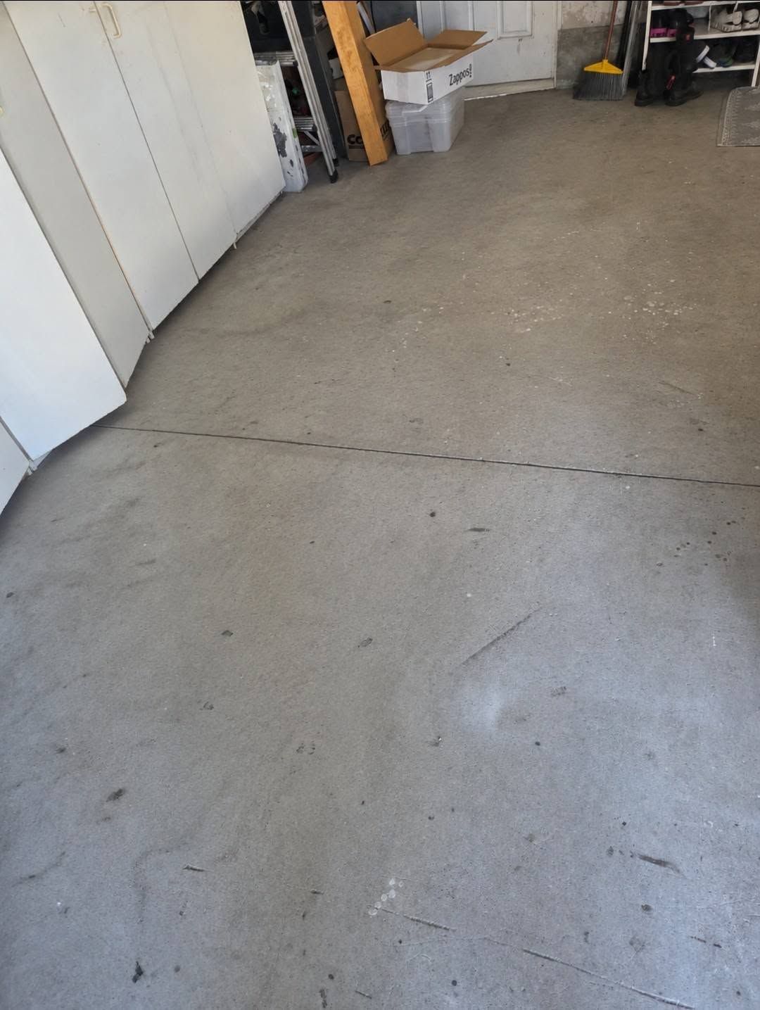 Concrete garage floor with a crack line, white cabinets on the left, and storage items in the background