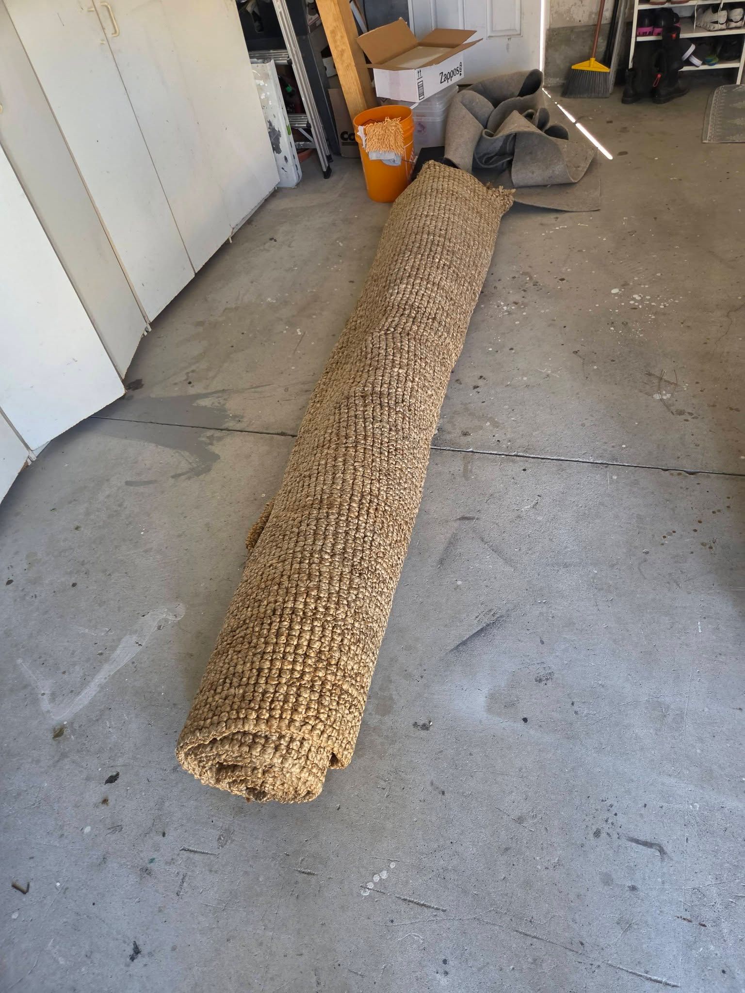 Long woven roll rug lying on a concrete garage floor with tools and bins in the background