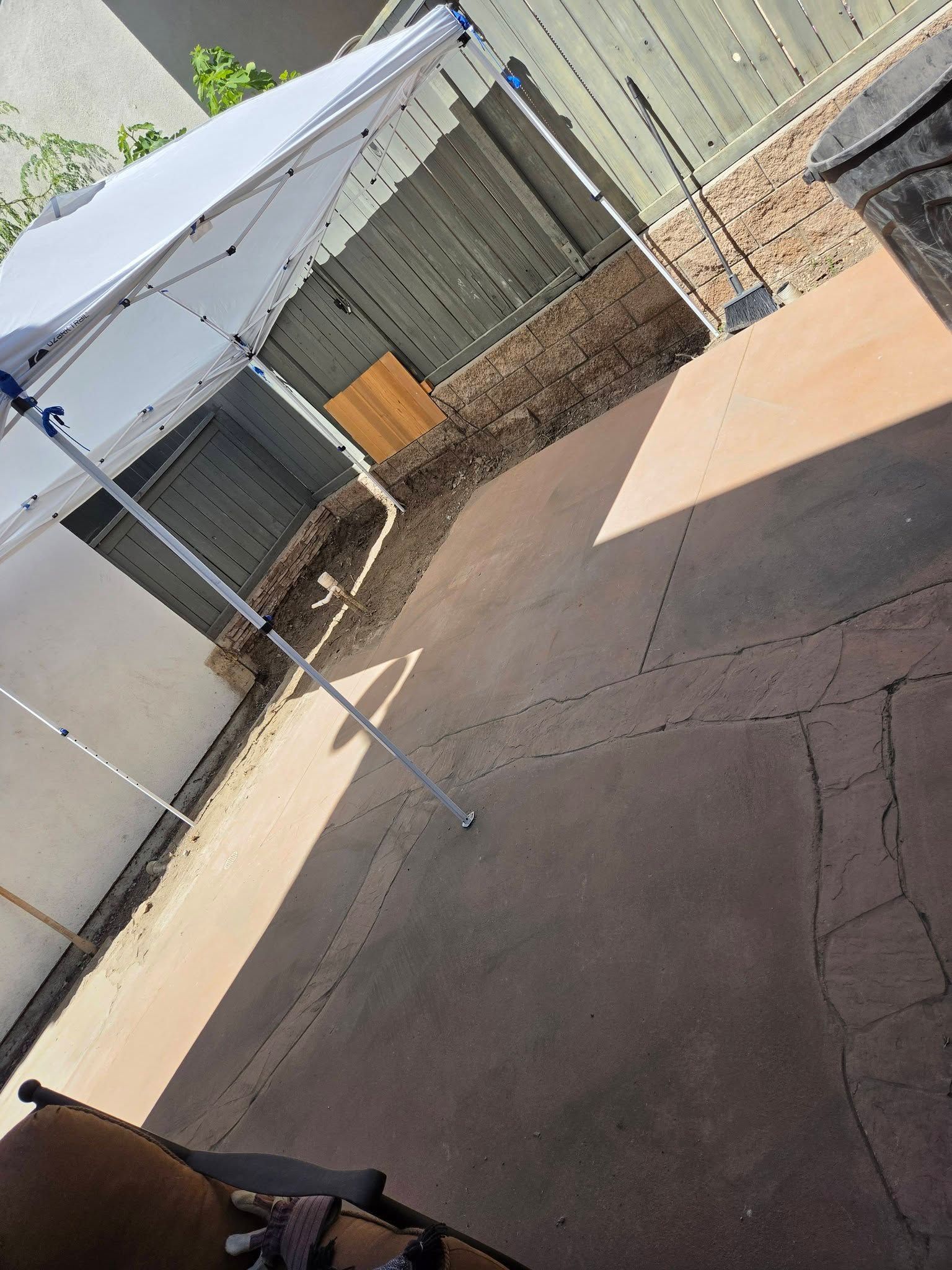 Tilted view of a backyard patio with concrete ground, a white canopy, fence, and shed