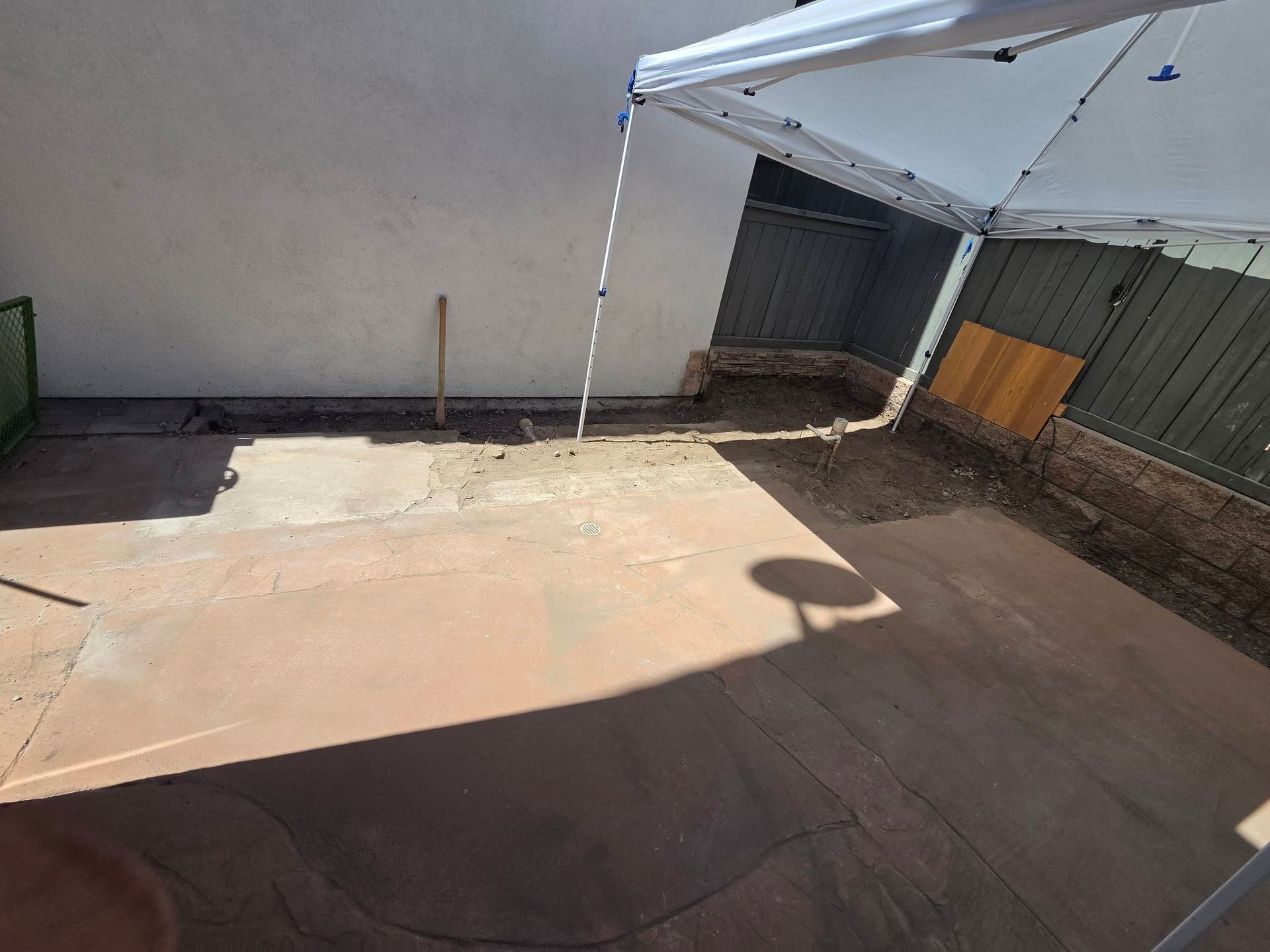 Empty concrete patio with a white canopy casting shadows beside a wall and garage door.