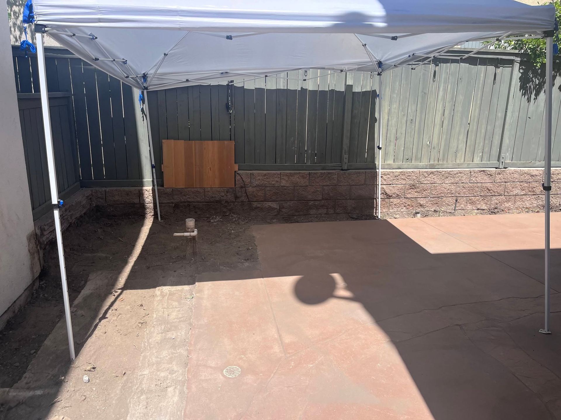Backyard patio under a white canopy, with a wooden fence and a small table against the wall.