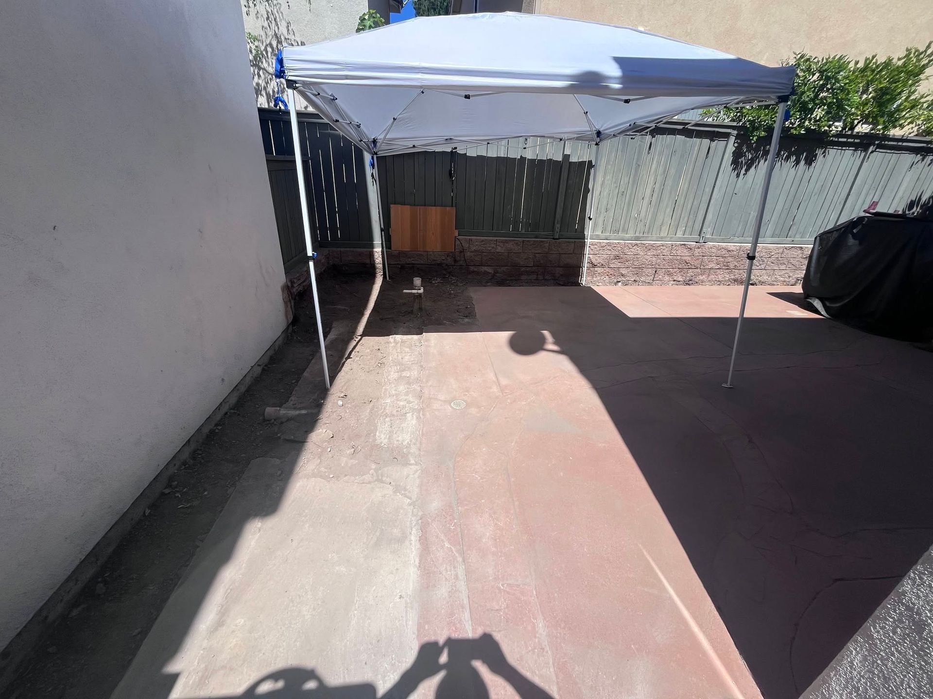 Empty backyard patio with a blue canopy tent and concrete wall shadows