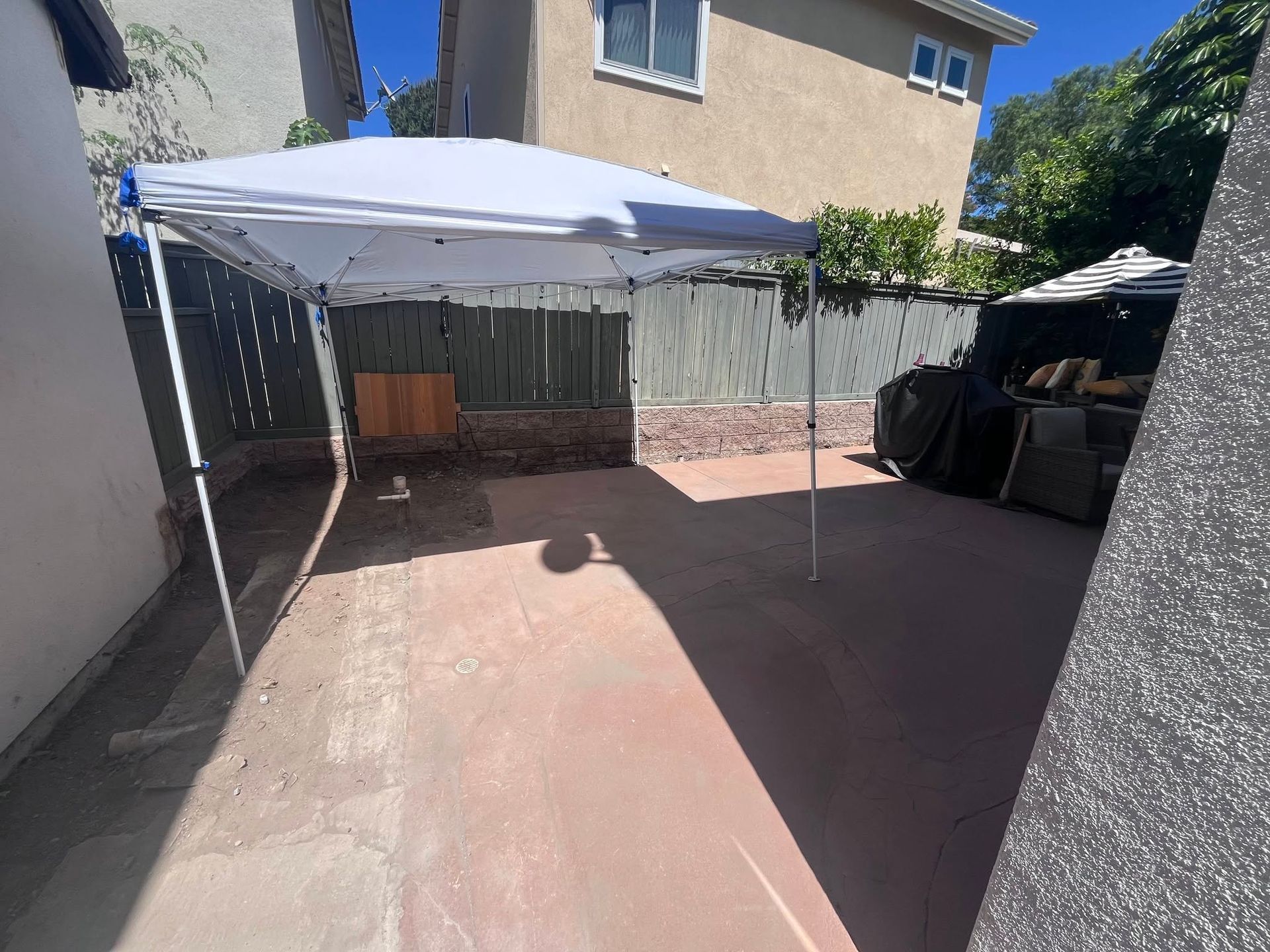 Backyard patio with a white canopy tent, concrete ground, and house wall in bright sunlight