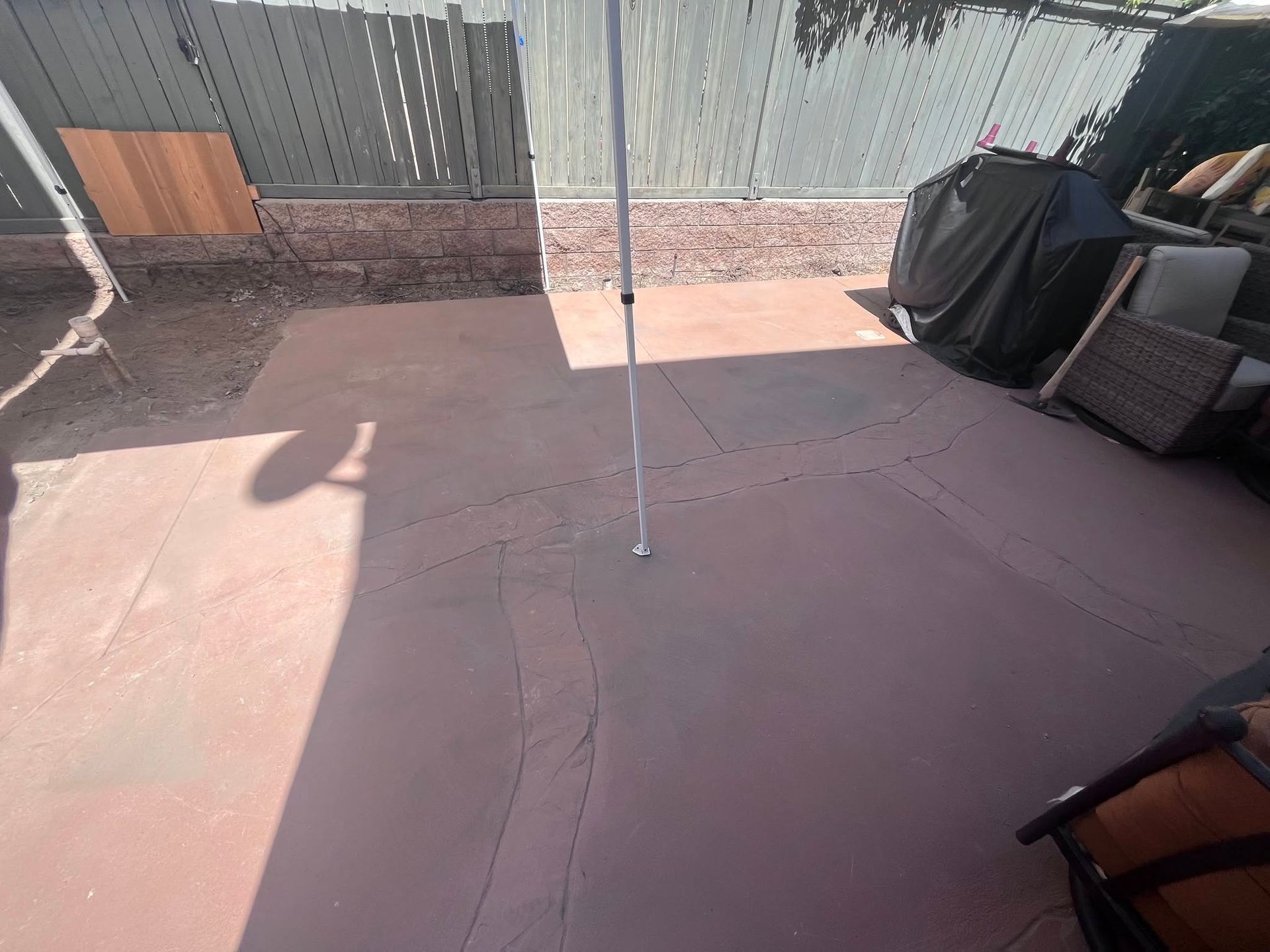 Backyard patio with pink tiles, a central pole, and covered furniture against a fence.
