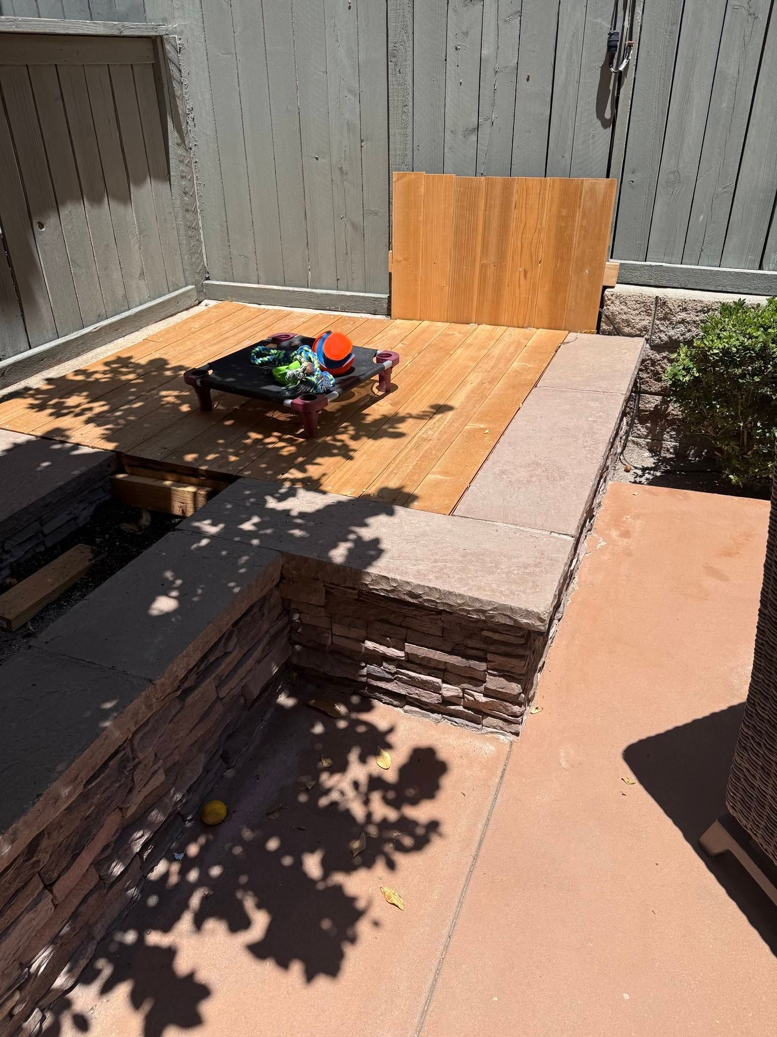 Outdoor patio with tiered concrete steps, a small garden bed, and a wooden fence in sunlight and shadows