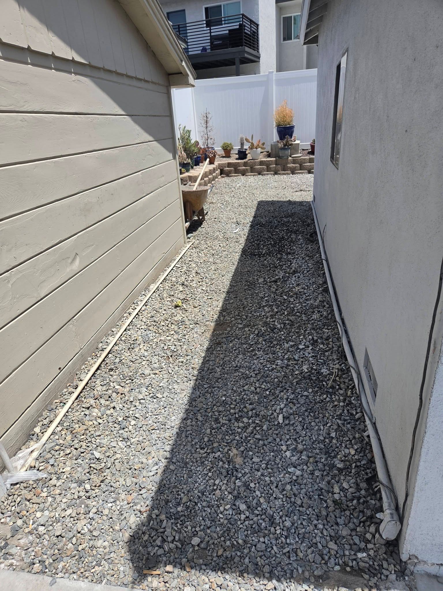 Narrow gravel walkway between two houses, with a person in the distance near the end.