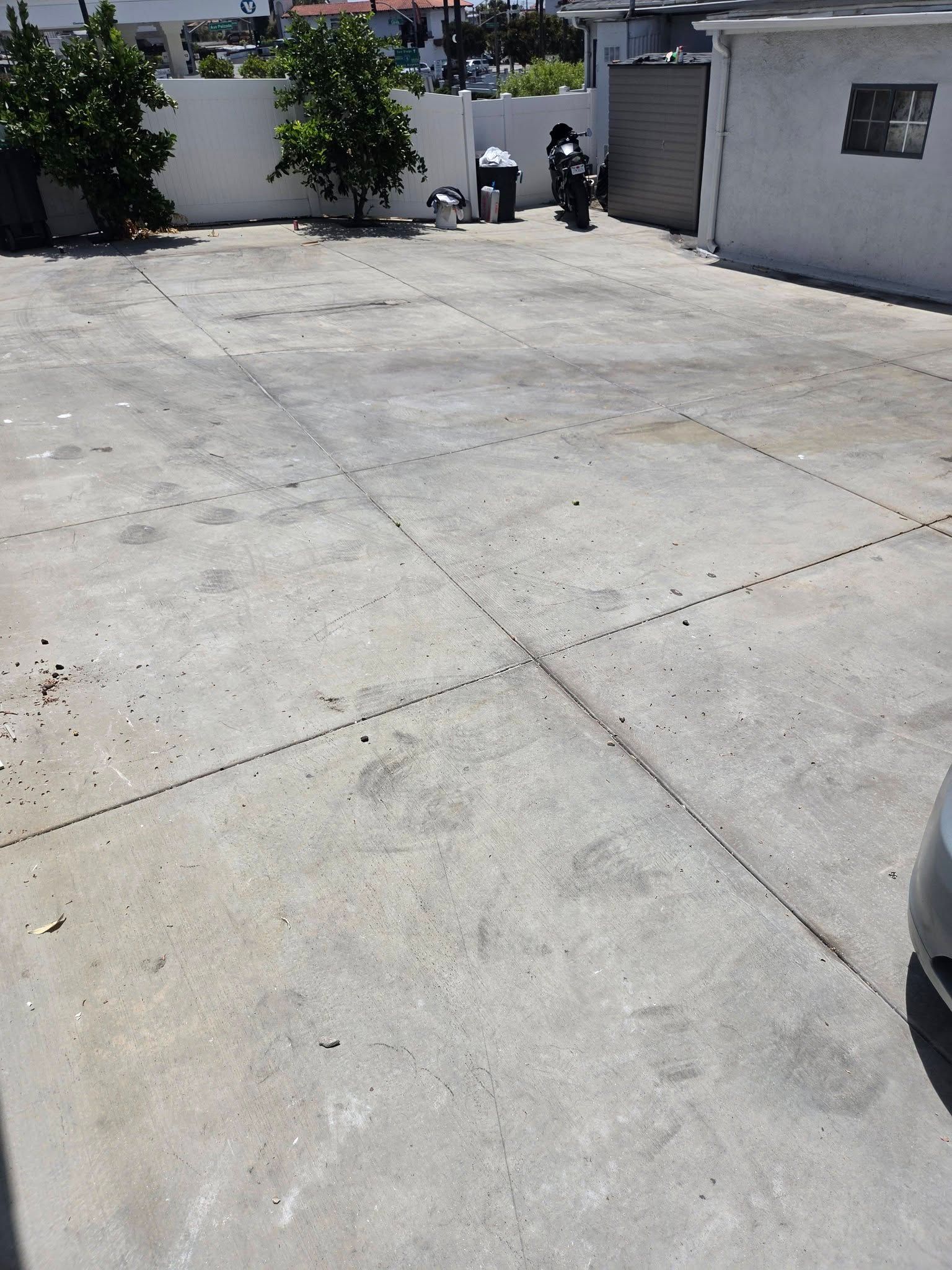 Sunlit concrete driveway beside a white wall, with two people near the back and a gray garage door.