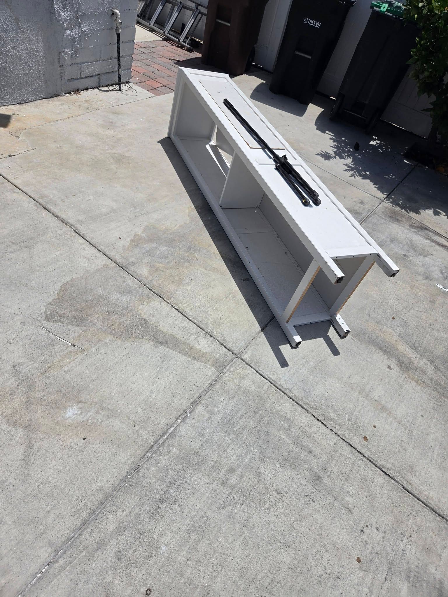 White countertop or shelf unit on a sunlit concrete patio beside a gray brick wall and dark doors