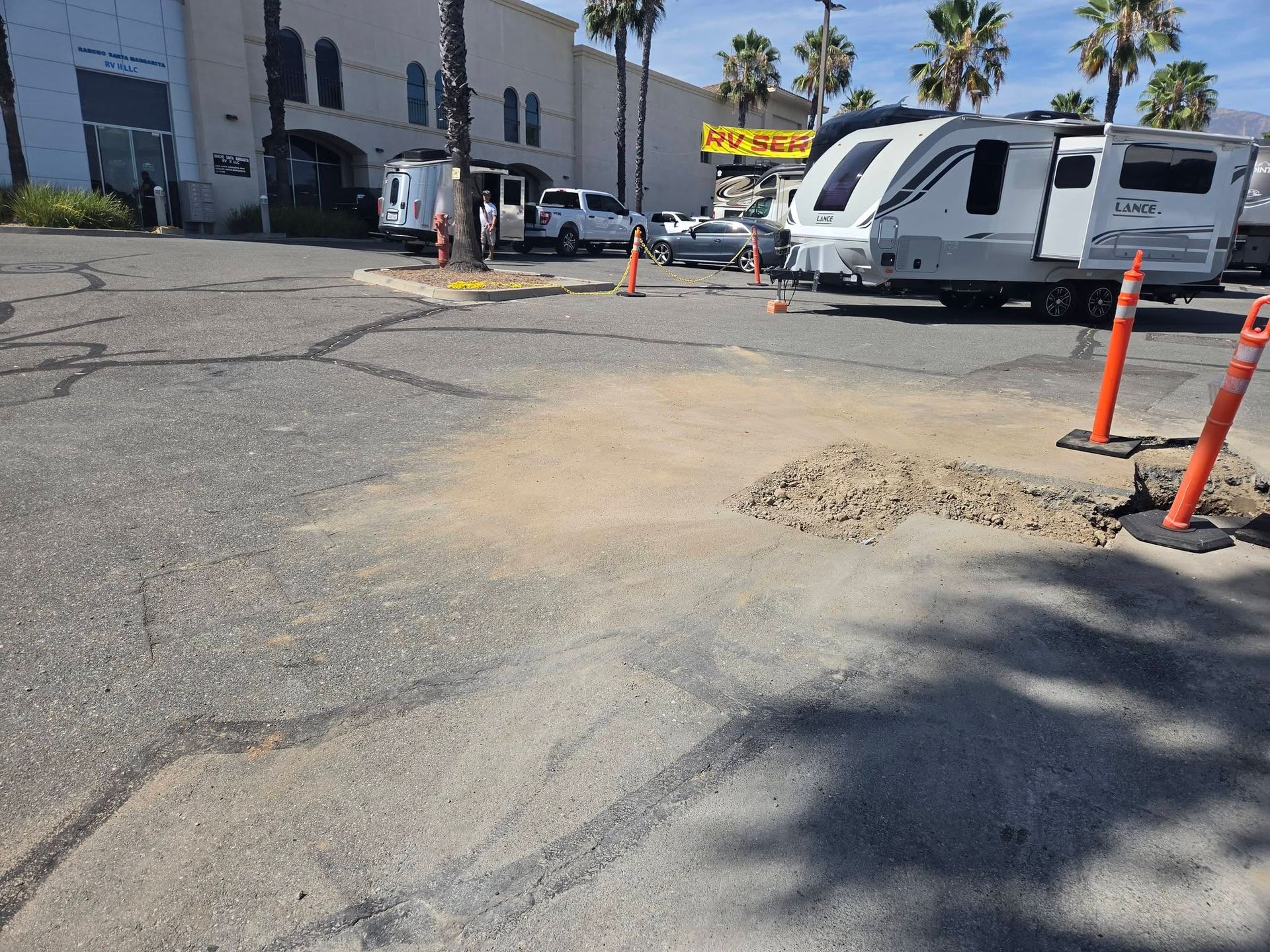 Parking lot with RVs, traffic cones, and a patched asphalt pothole under bright sun