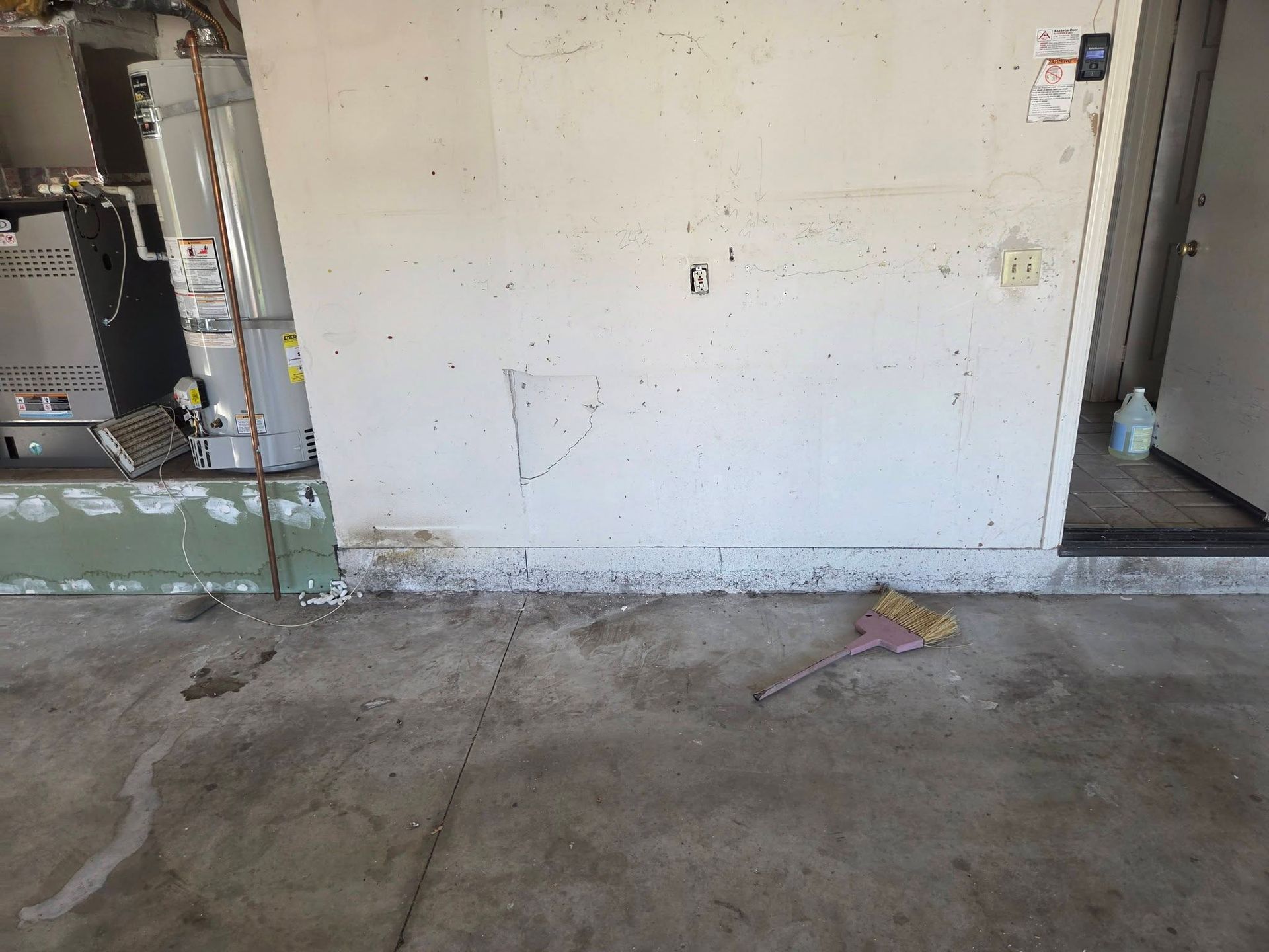 Empty unfinished room with concrete floor, white wall, exposed utility equipment, and doorway on the right