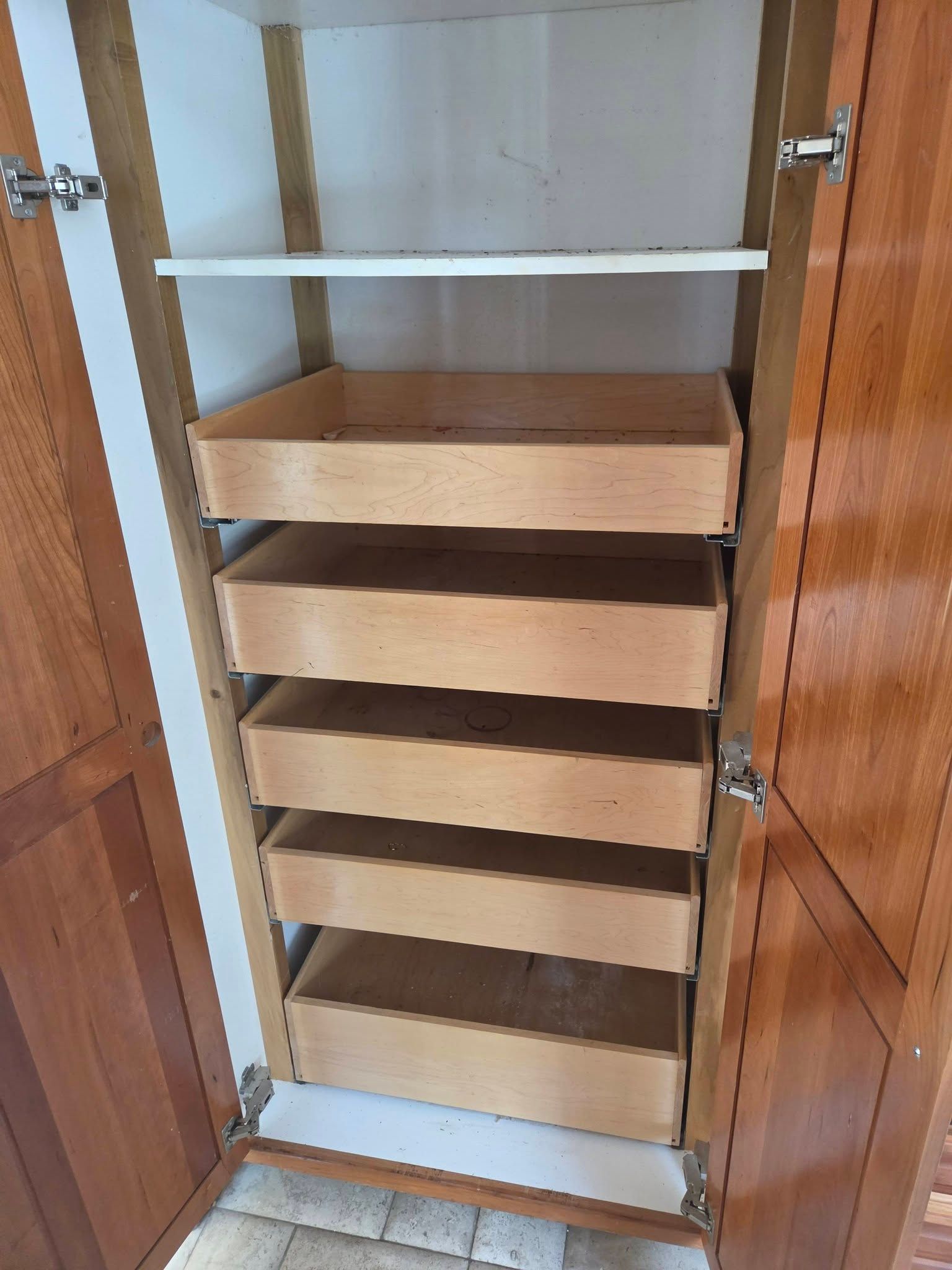 Open cabinet with five wooden pull-out drawers and white shelves inside.