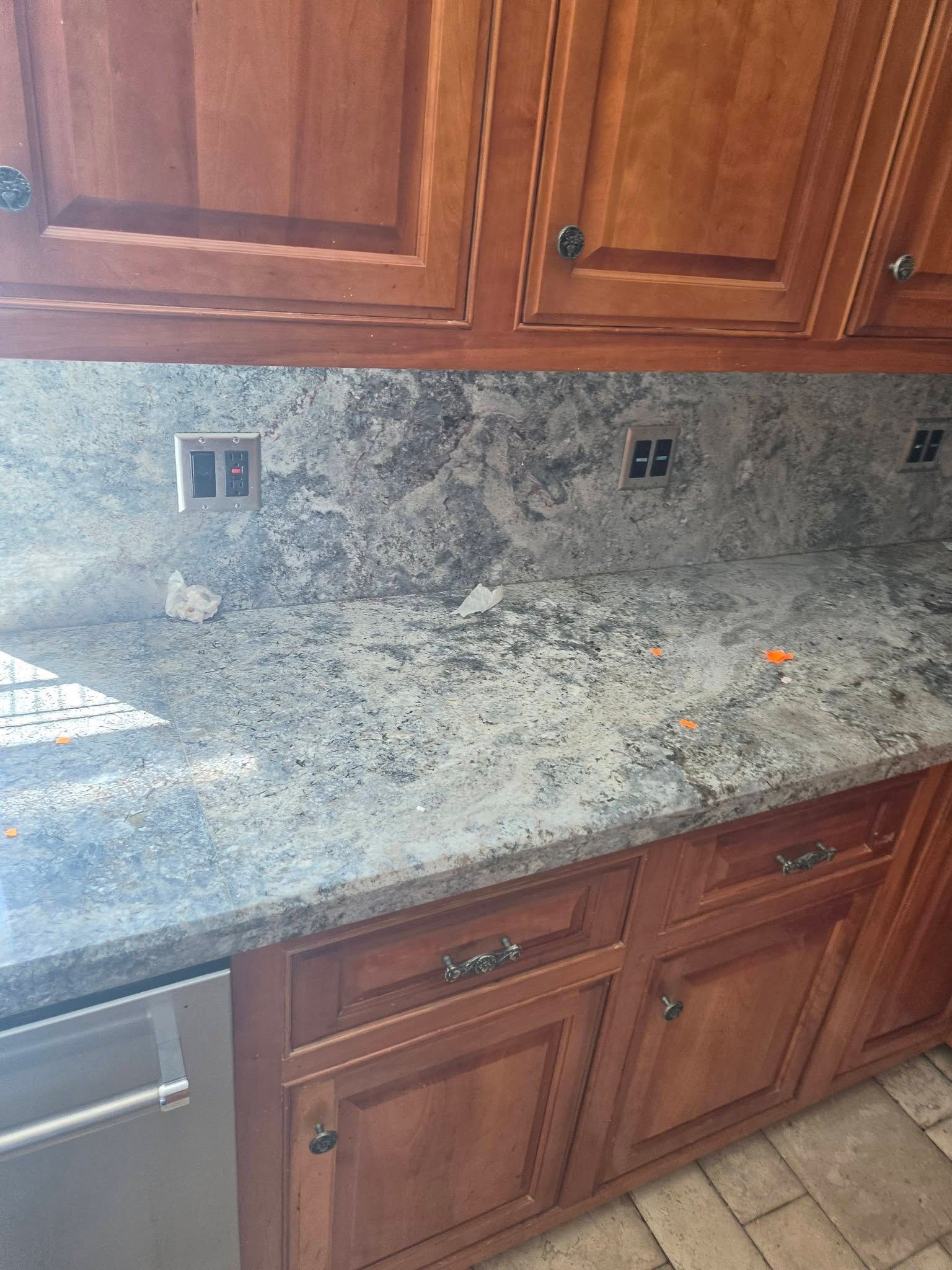 Kitchen countertop with speckled granite, wooden cabinets, and wall outlets beneath upper cabinets