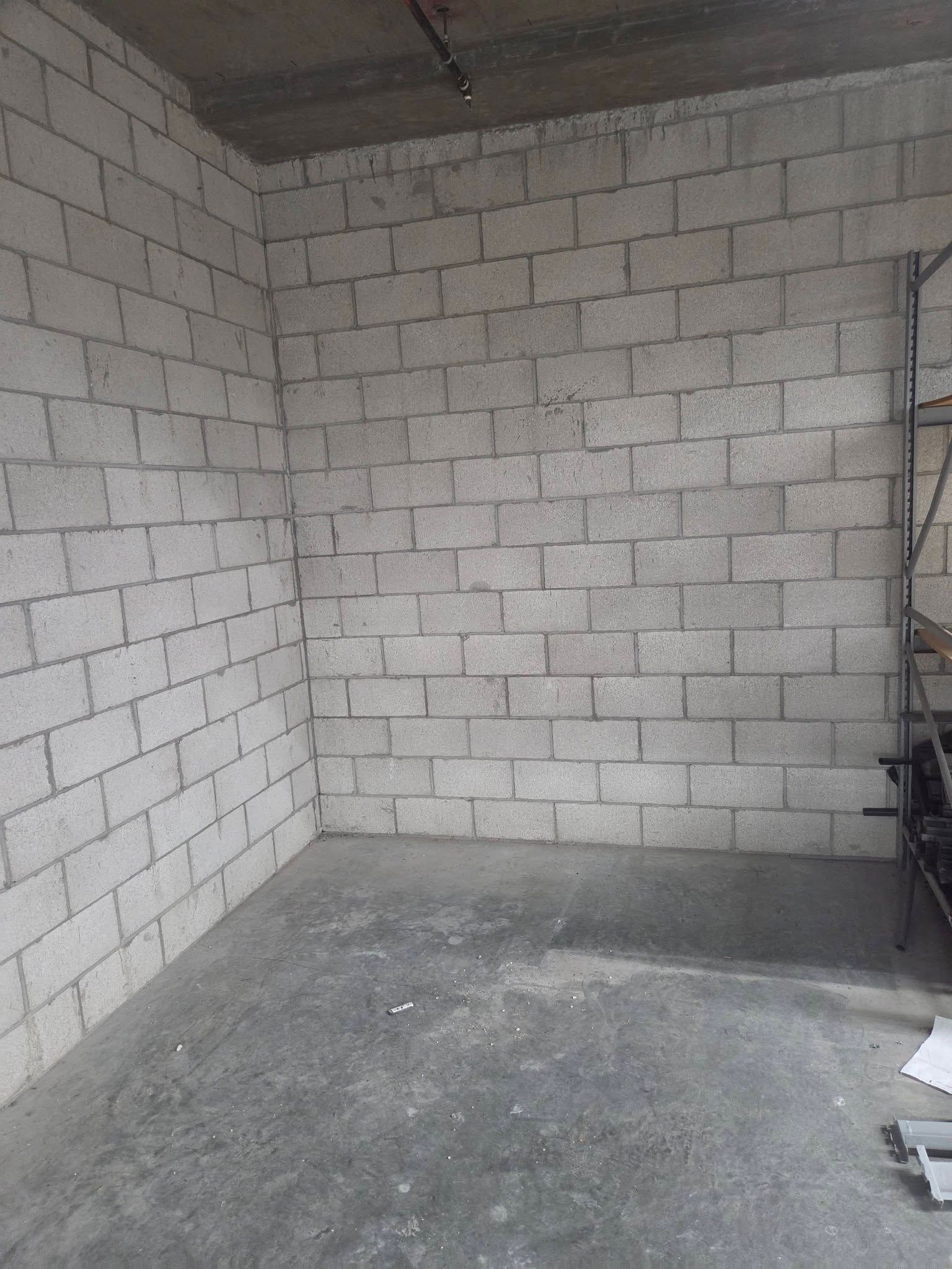 Empty cinder block room with gray floor and metal shelving on the right.