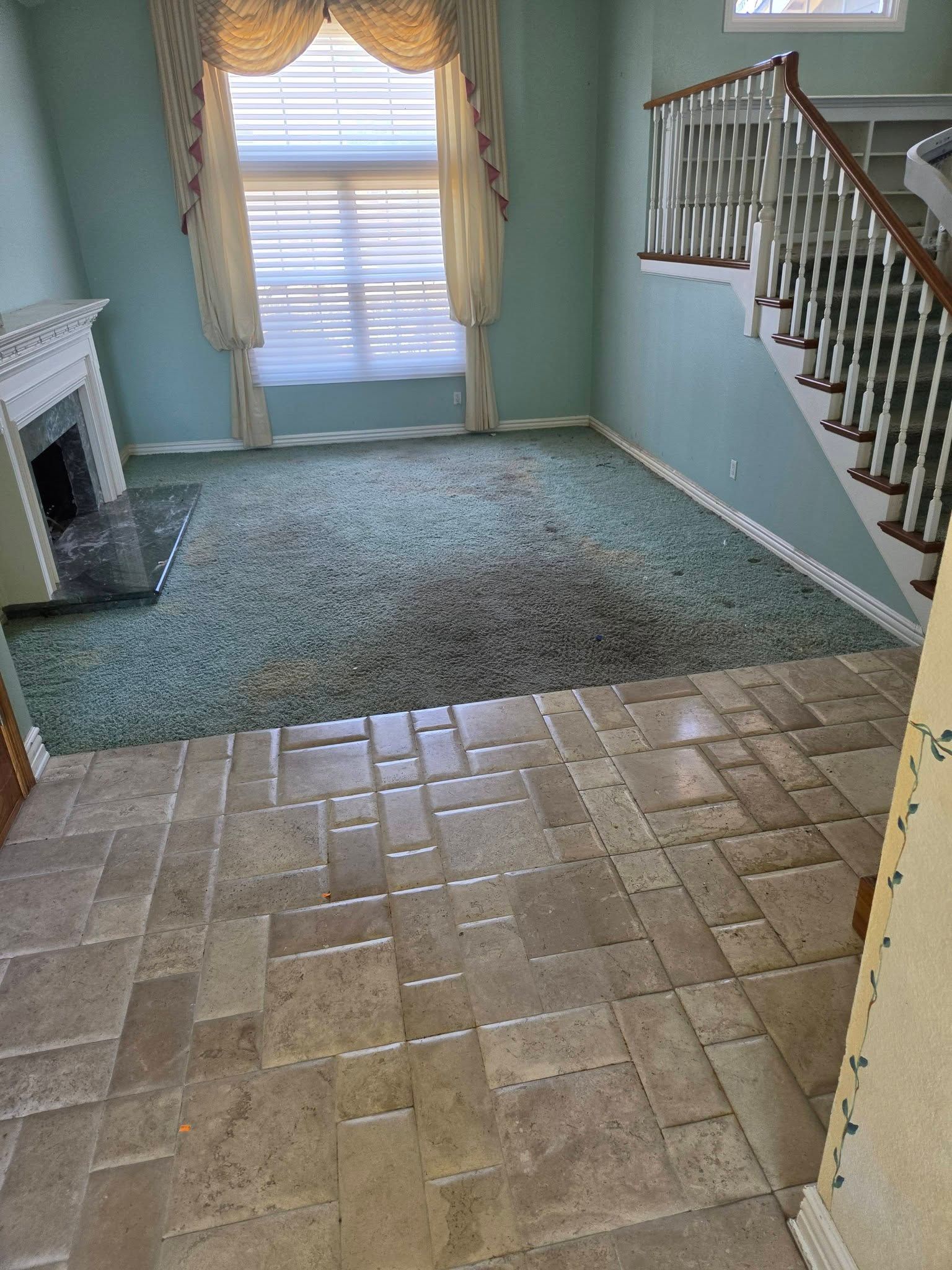 Interior room with tiled floor, green carpet, staircase, fireplace, and window with curtains
