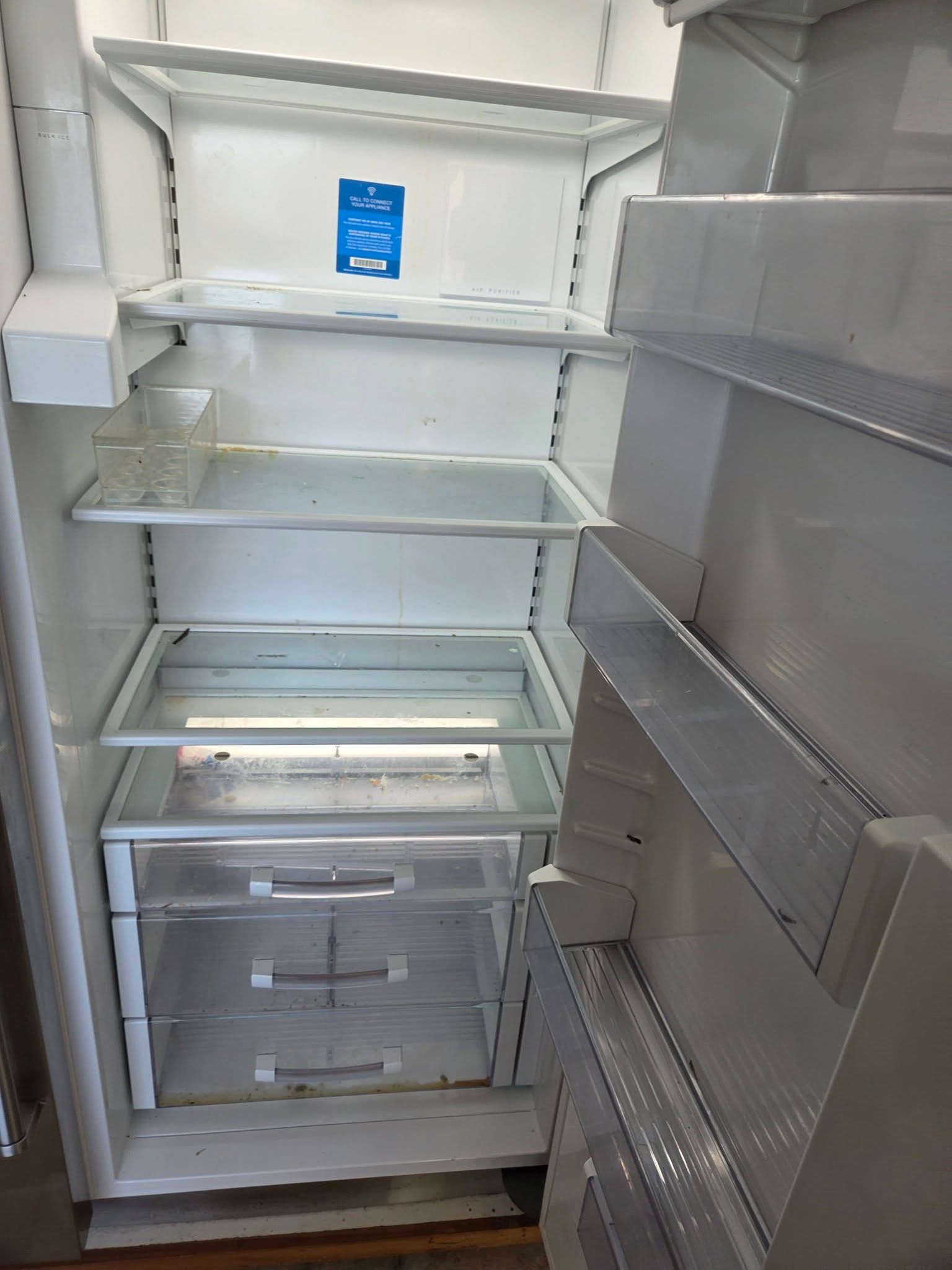 Empty white refrigerator with glass shelves and a freezer drawer, door open.