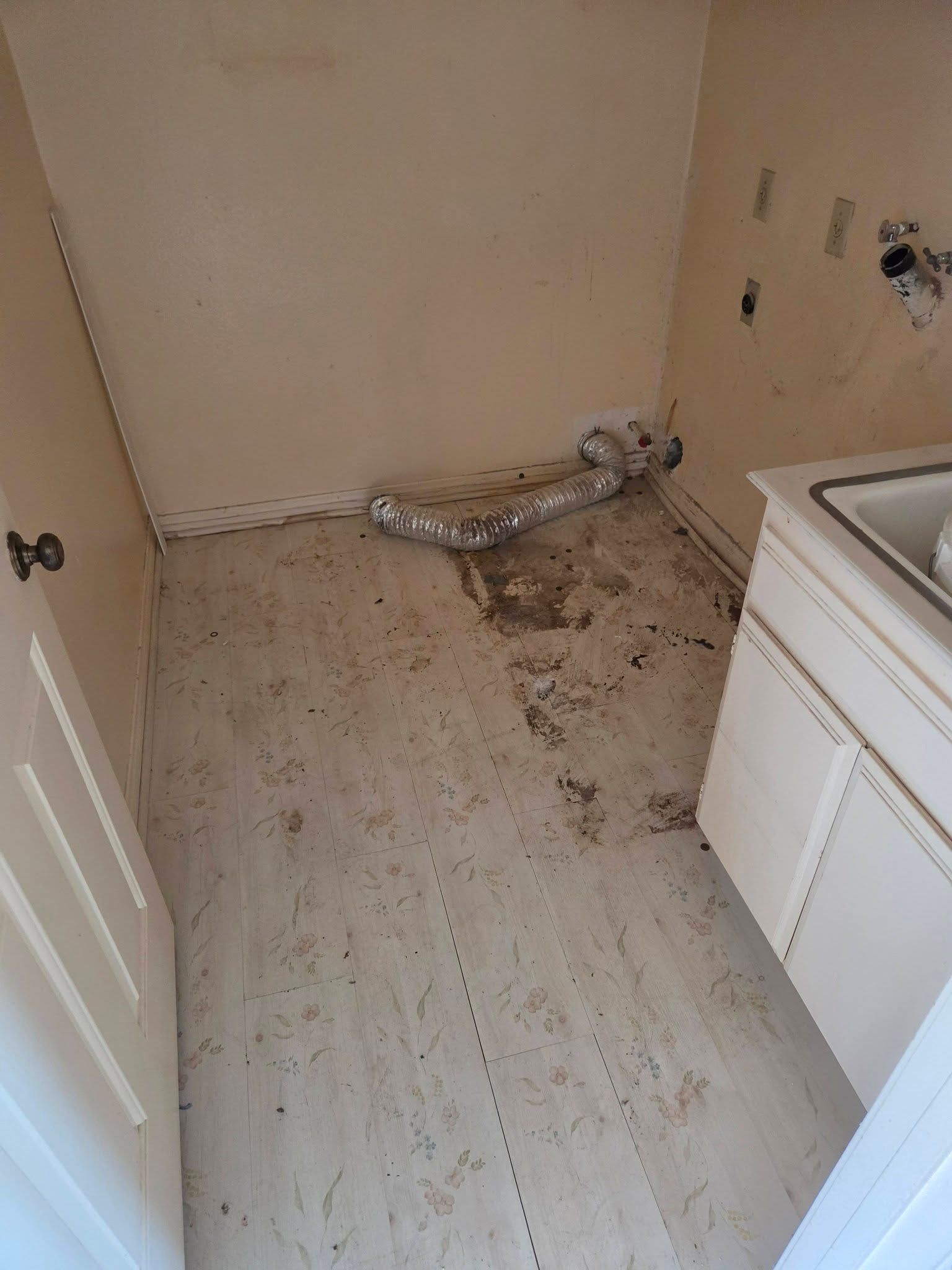 Dirty laundry room floor with scattered debris and a disconnected silver duct near the wall.