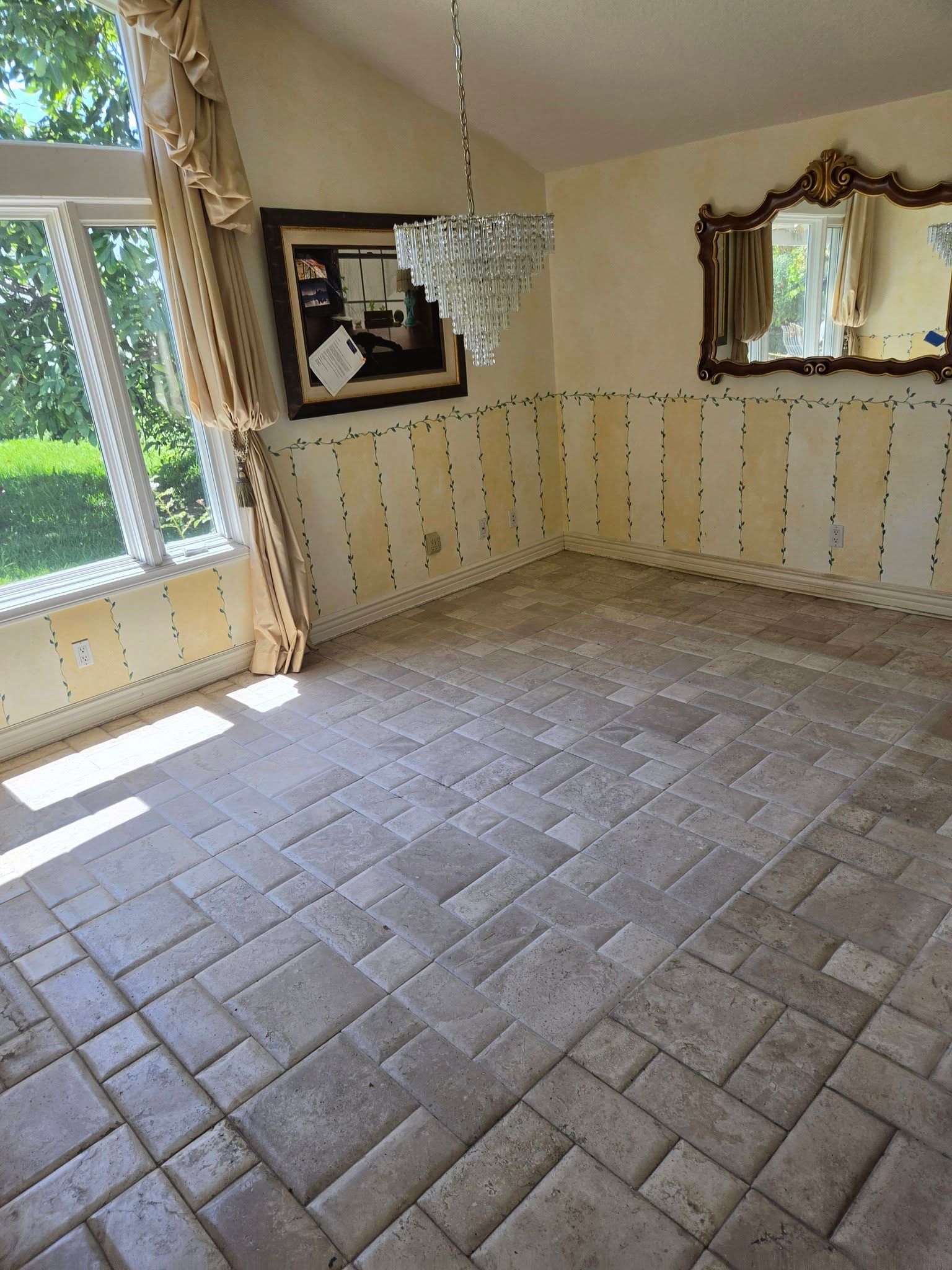 Empty room with tile floor, white paneled walls, and large window with curtains and a mirror