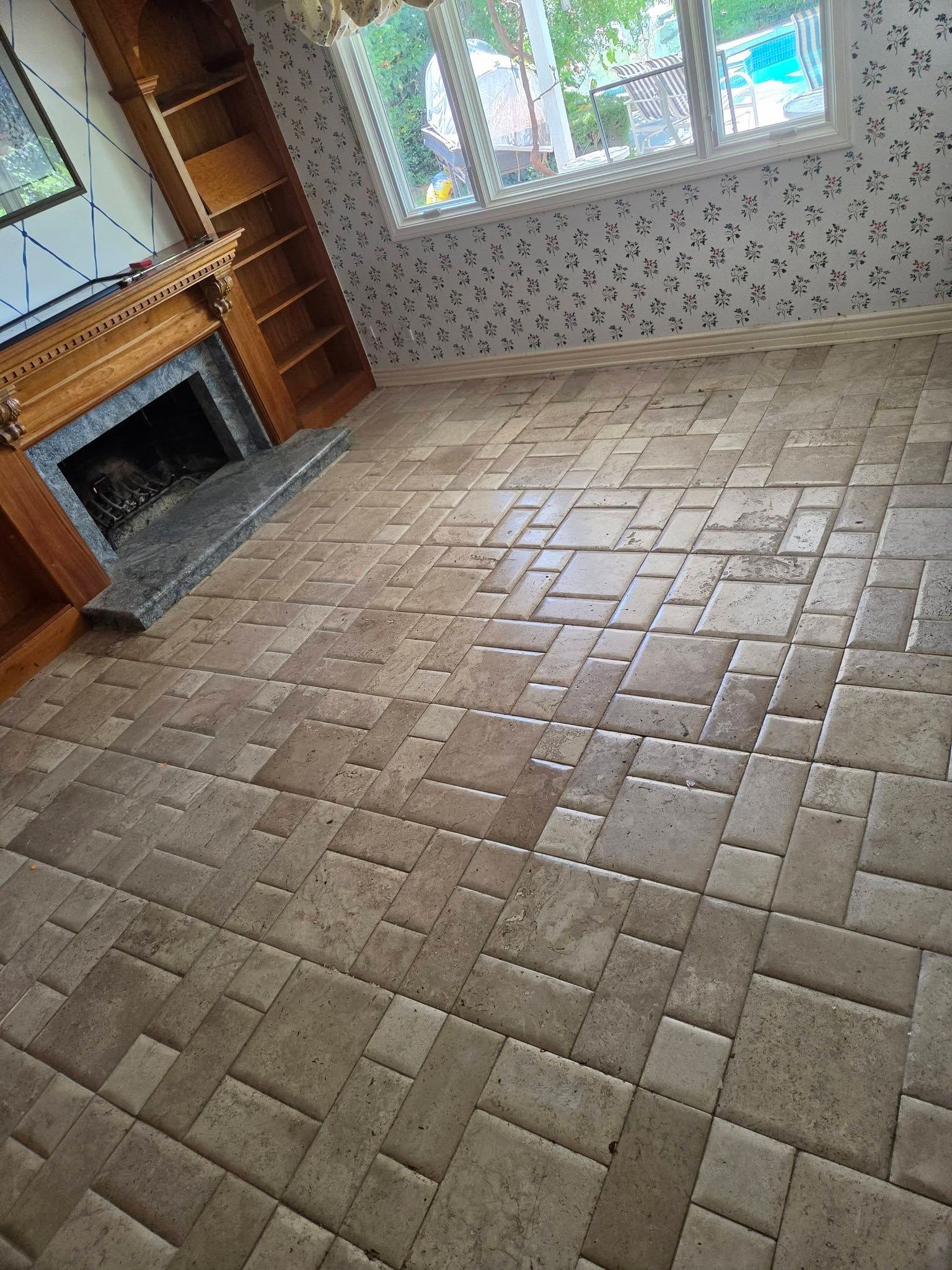 Empty living room with tiled floor, fireplace, wood shelves, and large windows.