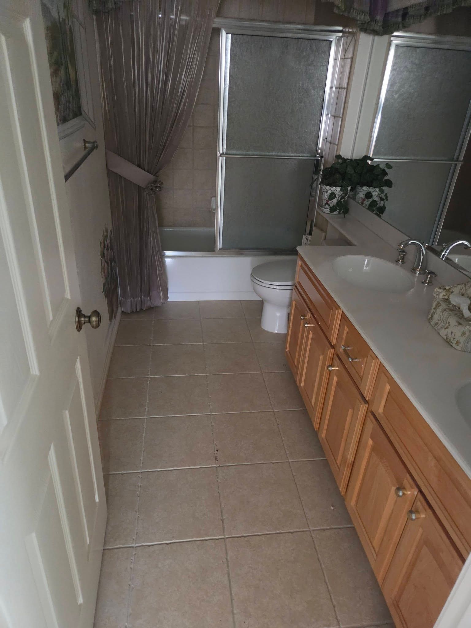 Narrow bathroom with beige tile, wooden vanity, white toilet, and frosted glass windows.