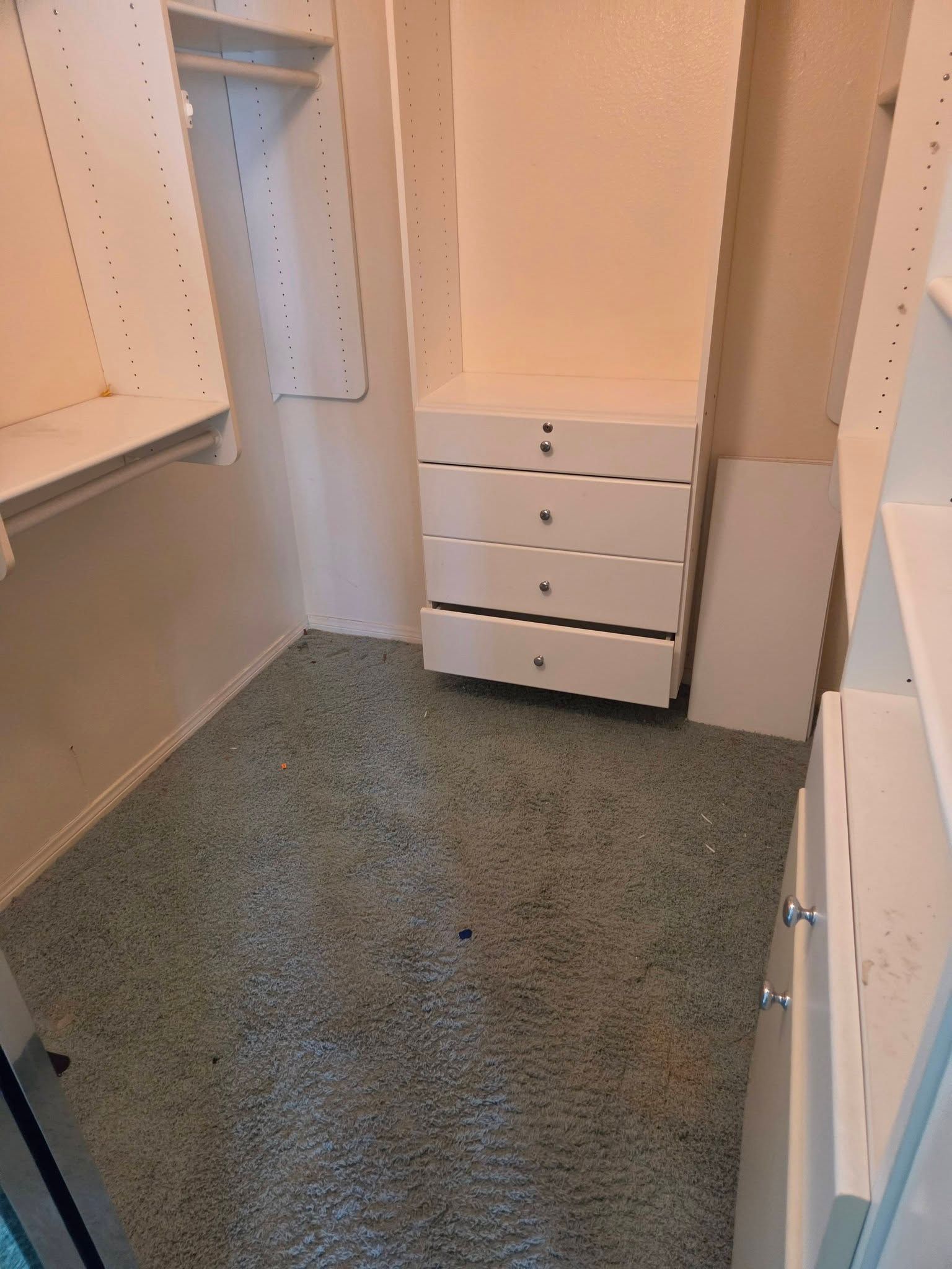 Empty walk-in closet with white shelves, drawers, and gray carpet.