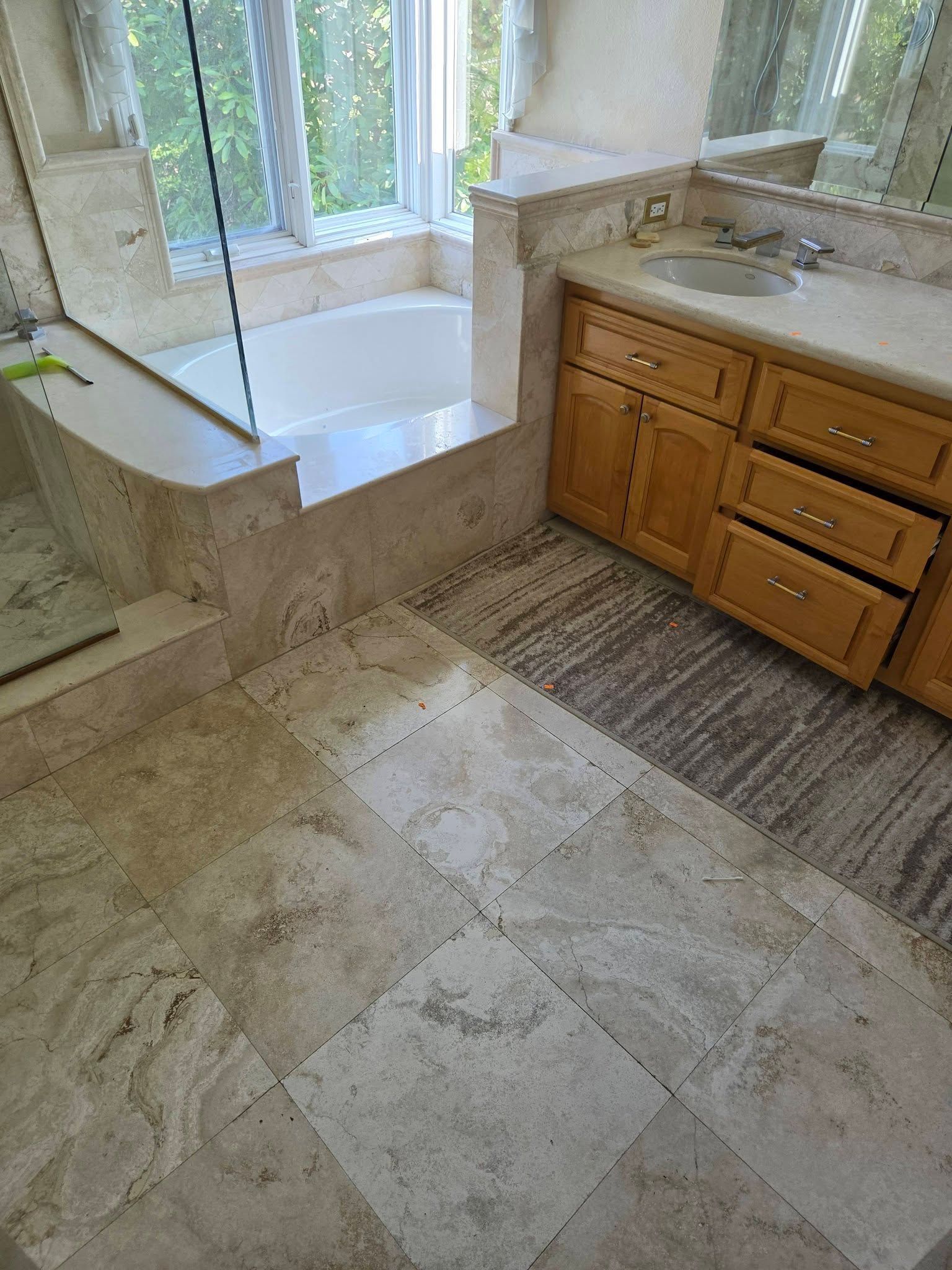 Bathroom with tiled floor, large window, corner bathtub, and wood vanity with sink.