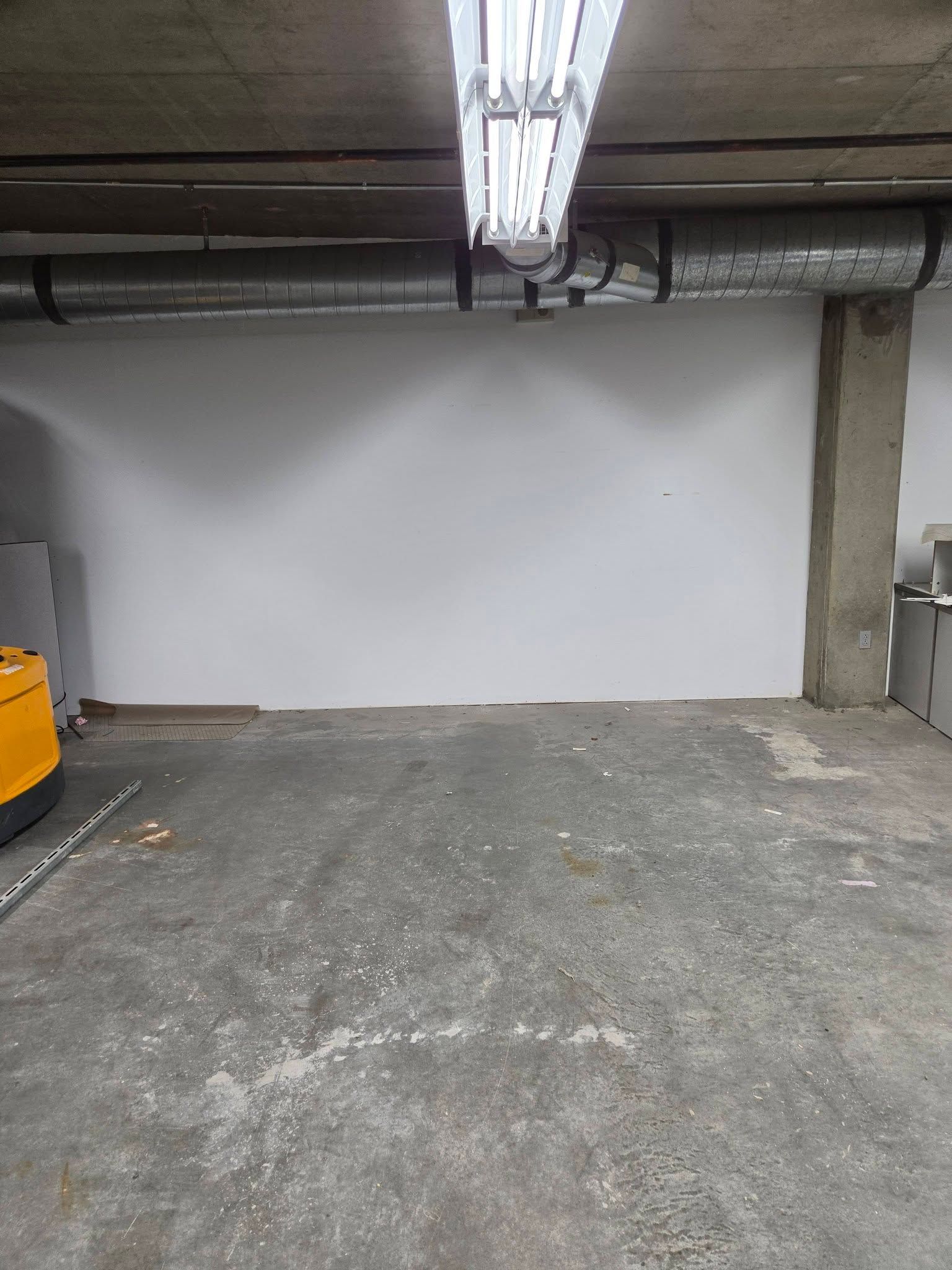 Empty concrete parking garage with a white wall and fluorescent ceiling lights