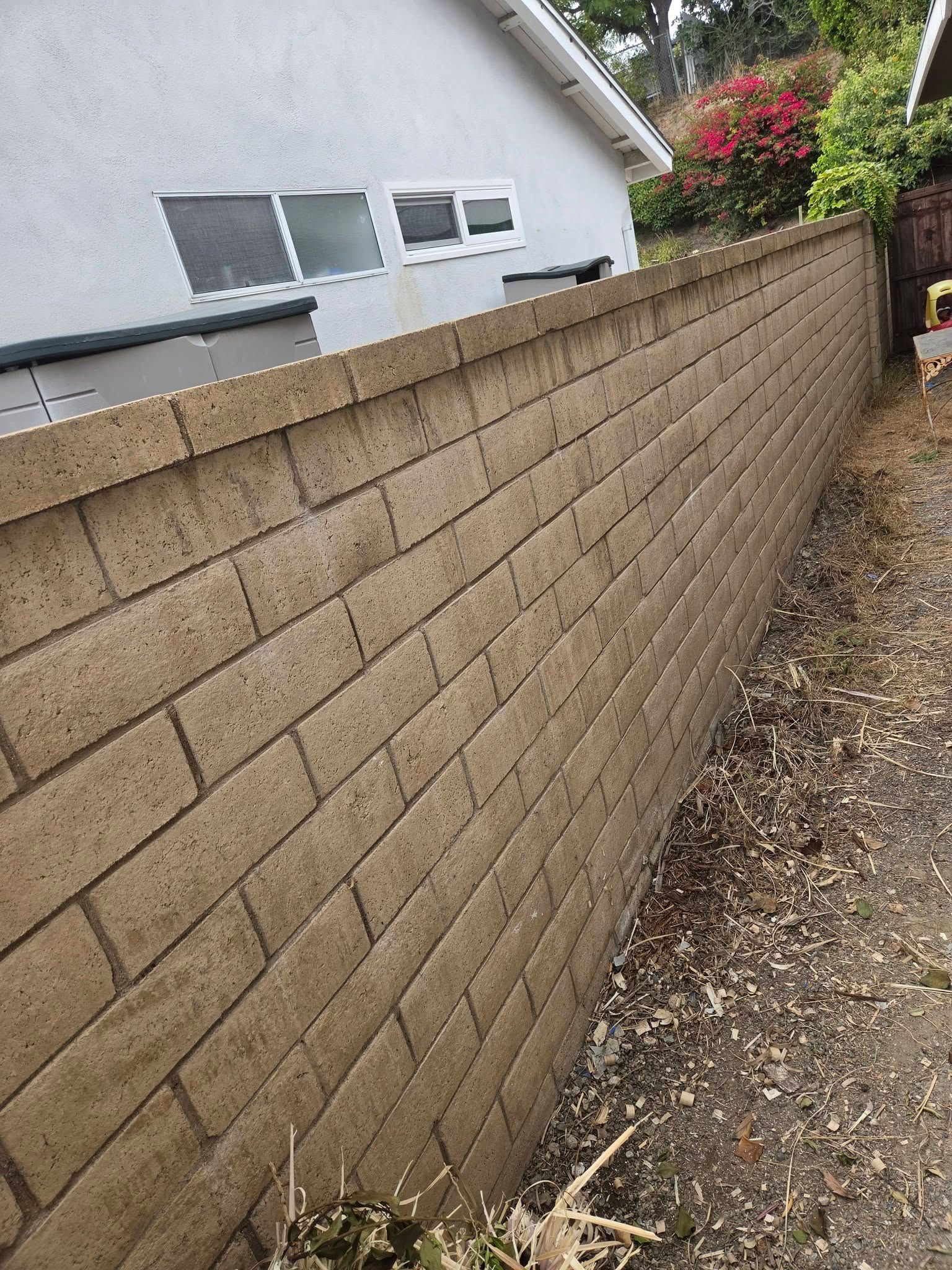 Sloped tan block retaining wall beside a gravel path and white house