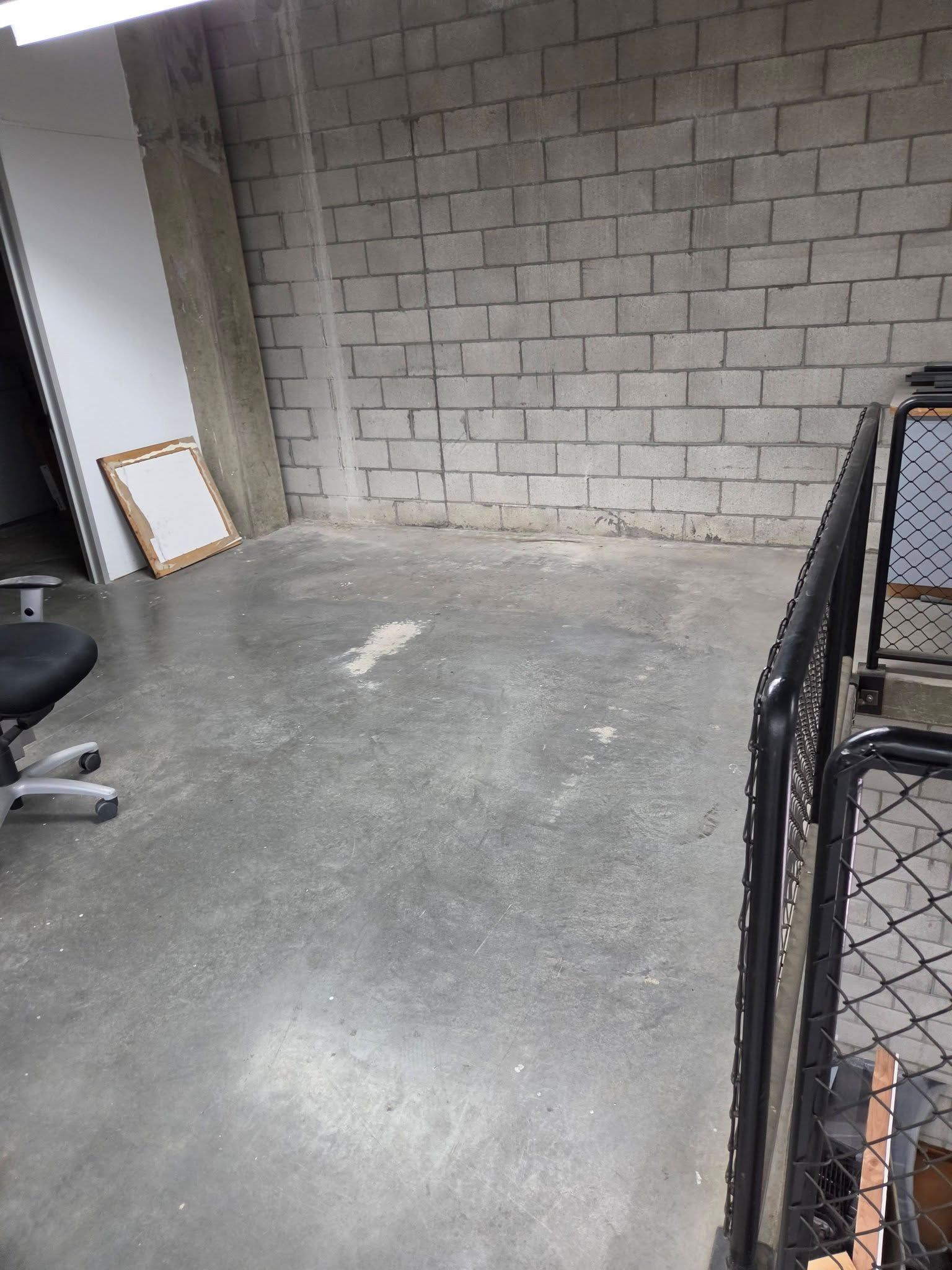 Empty unfinished room with cinderblock wall, concrete floor, and a chair at the left edge.