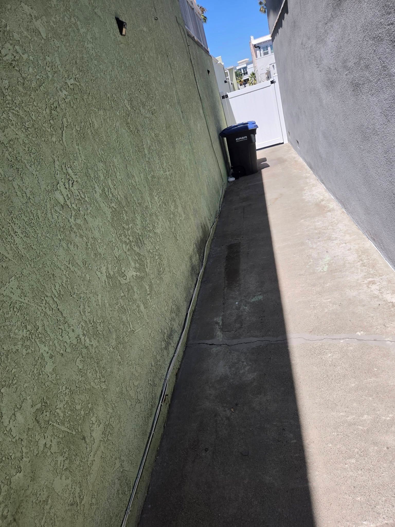 Narrow sunlit alley with green and white walls and a trash bin at the far end